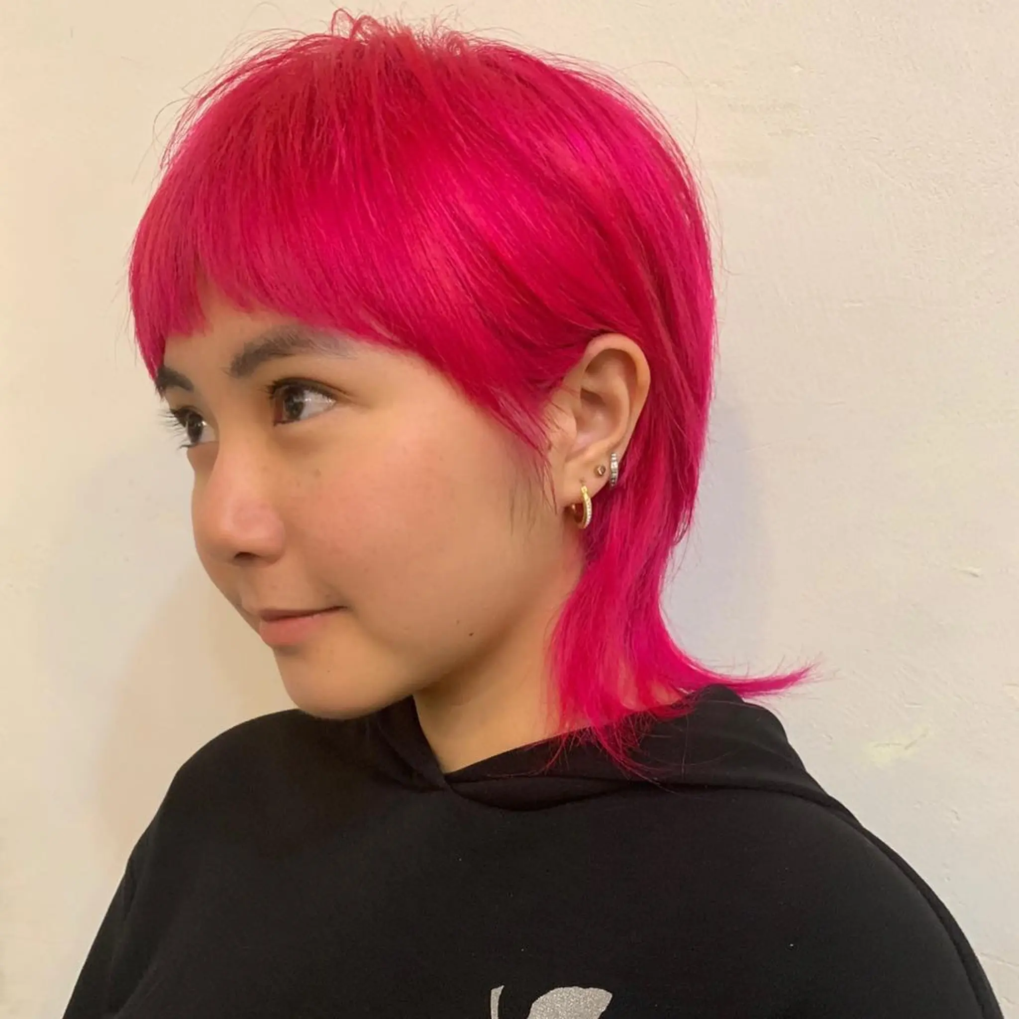 The hairstyle is a vibrant magenta, medium-length cut featuring straight hair with layers. It combines elements of a pixie and mullet style, with shorter choppy layers on top and longer, straighter locks at the back. The front has a short, blunt fringe that frames the face by Zen. 1