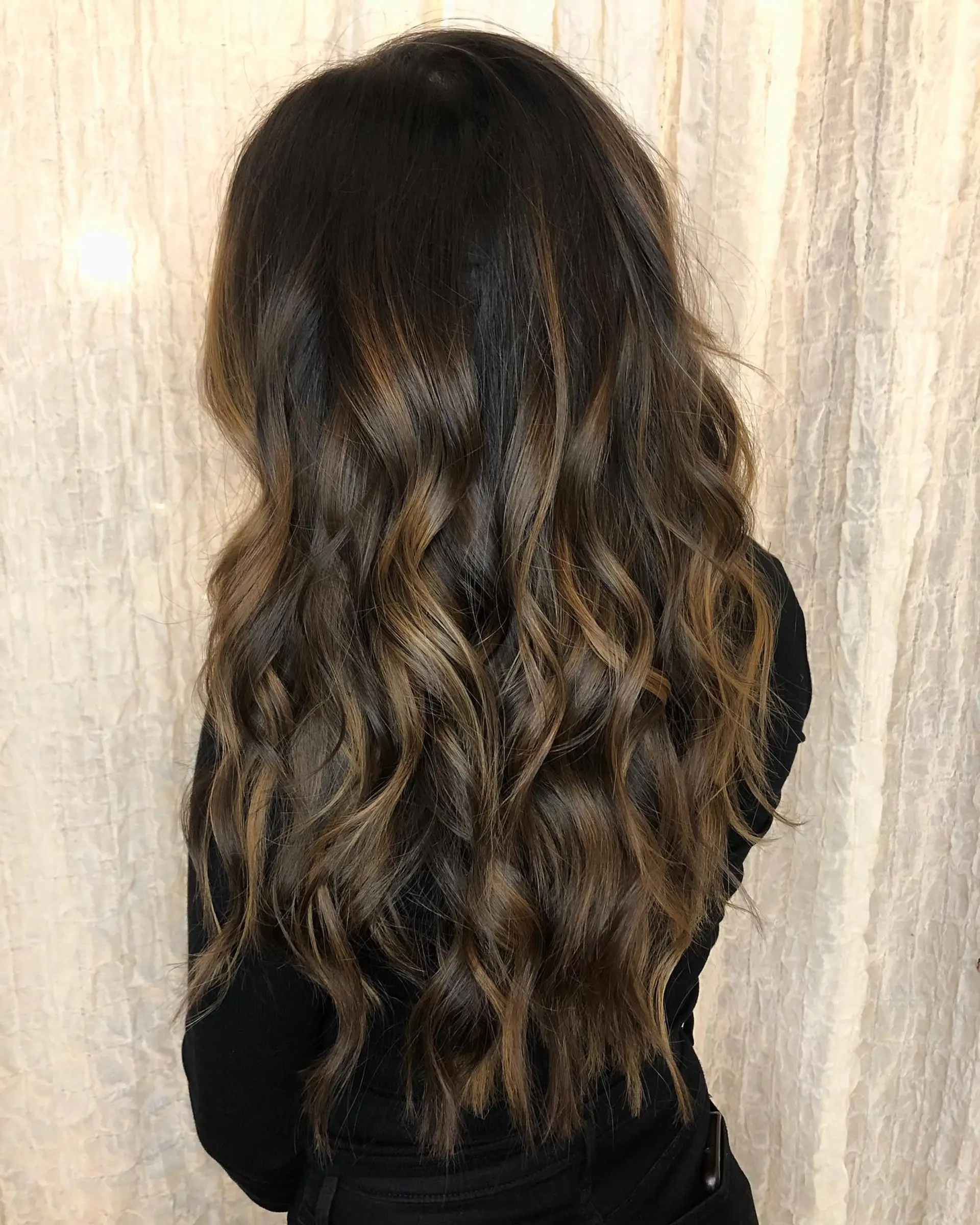 Long dark brown hair enhanced with seamless caramel balayage highlights and styled in relaxed, flowing waves. 1