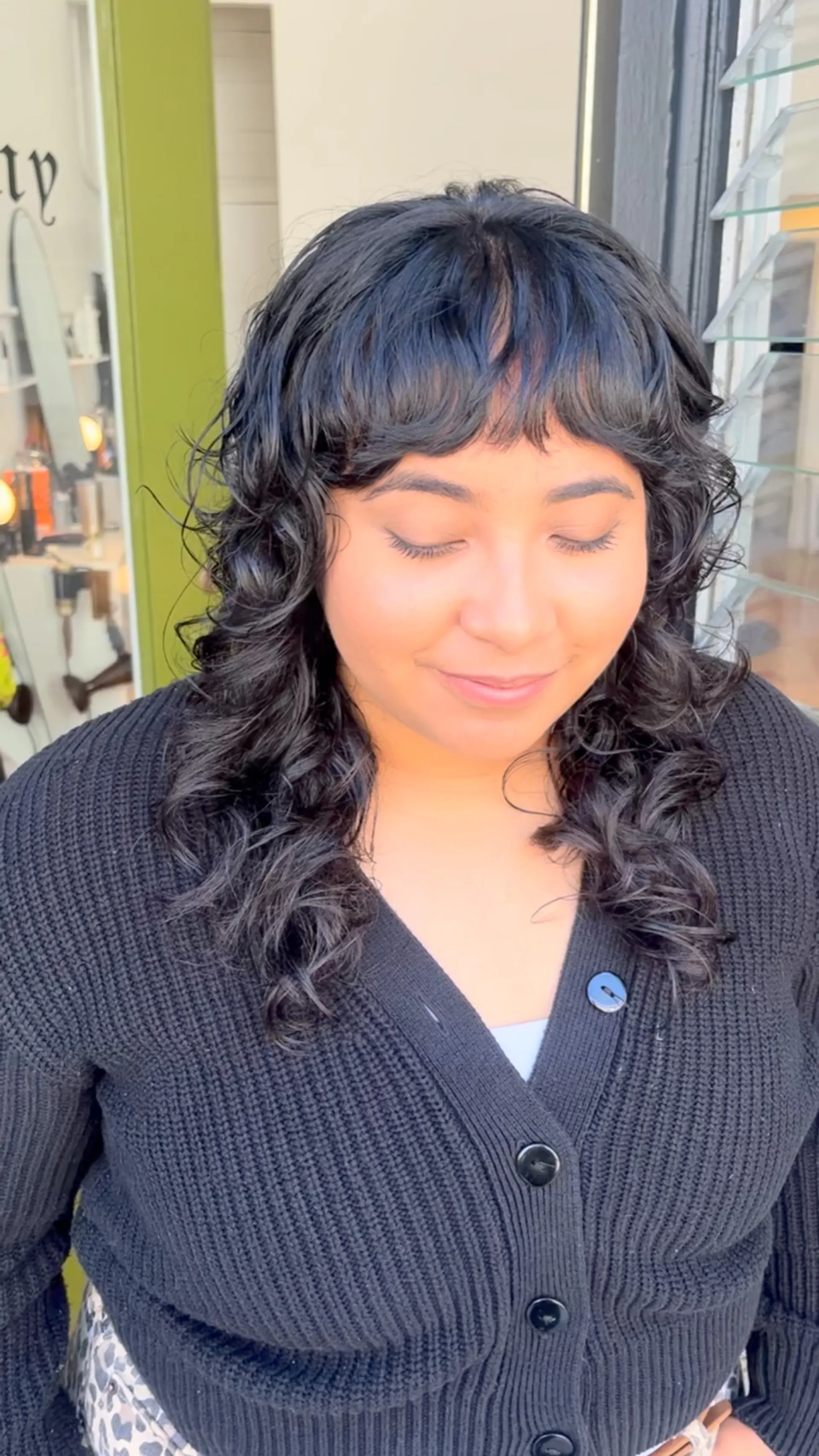 A textured curly shag haircut featuring wispy front bangs and layered definition around the shoulders. 1