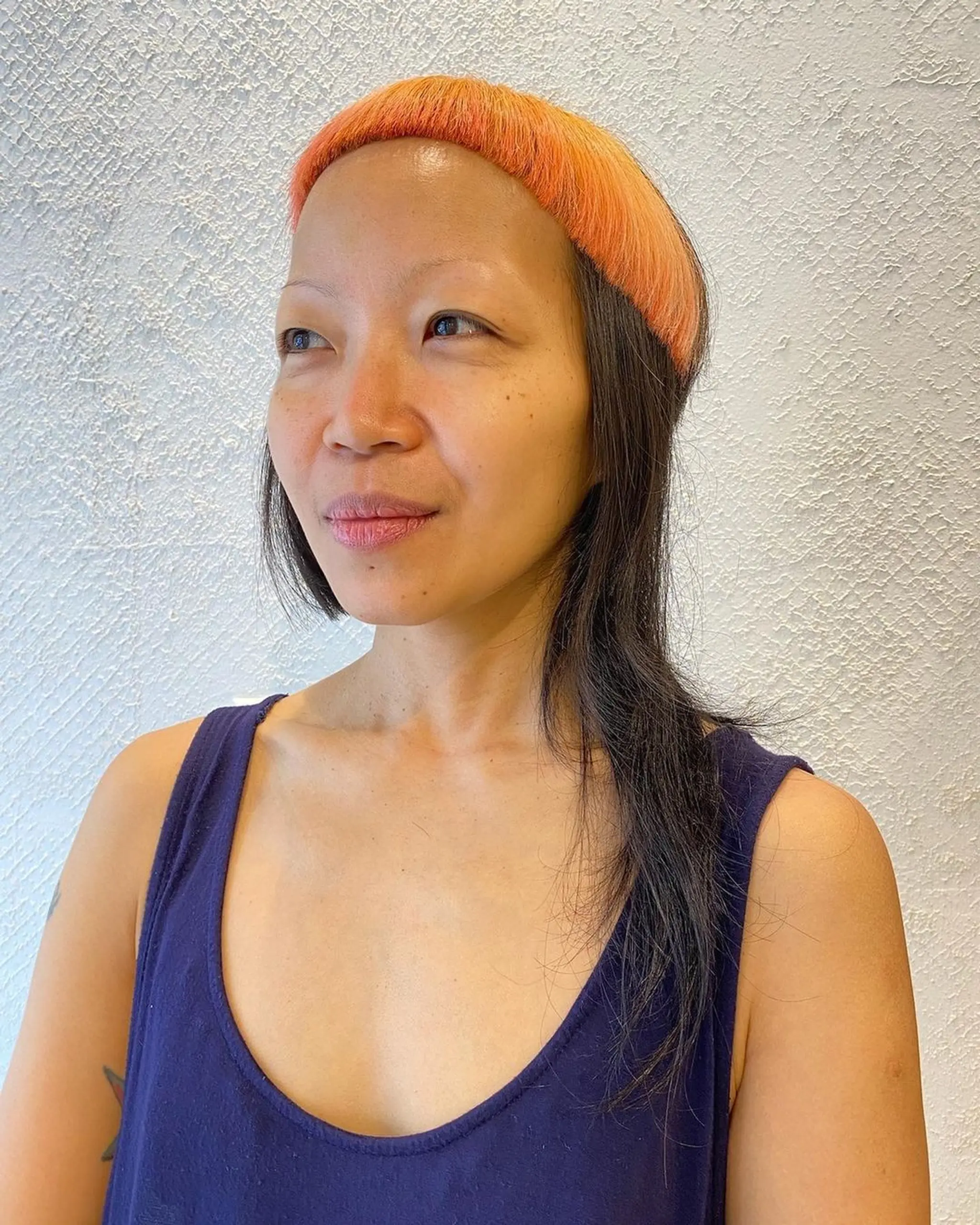 A hairstyle with vivid orange fringe and natural black, straight, medium-length hair.