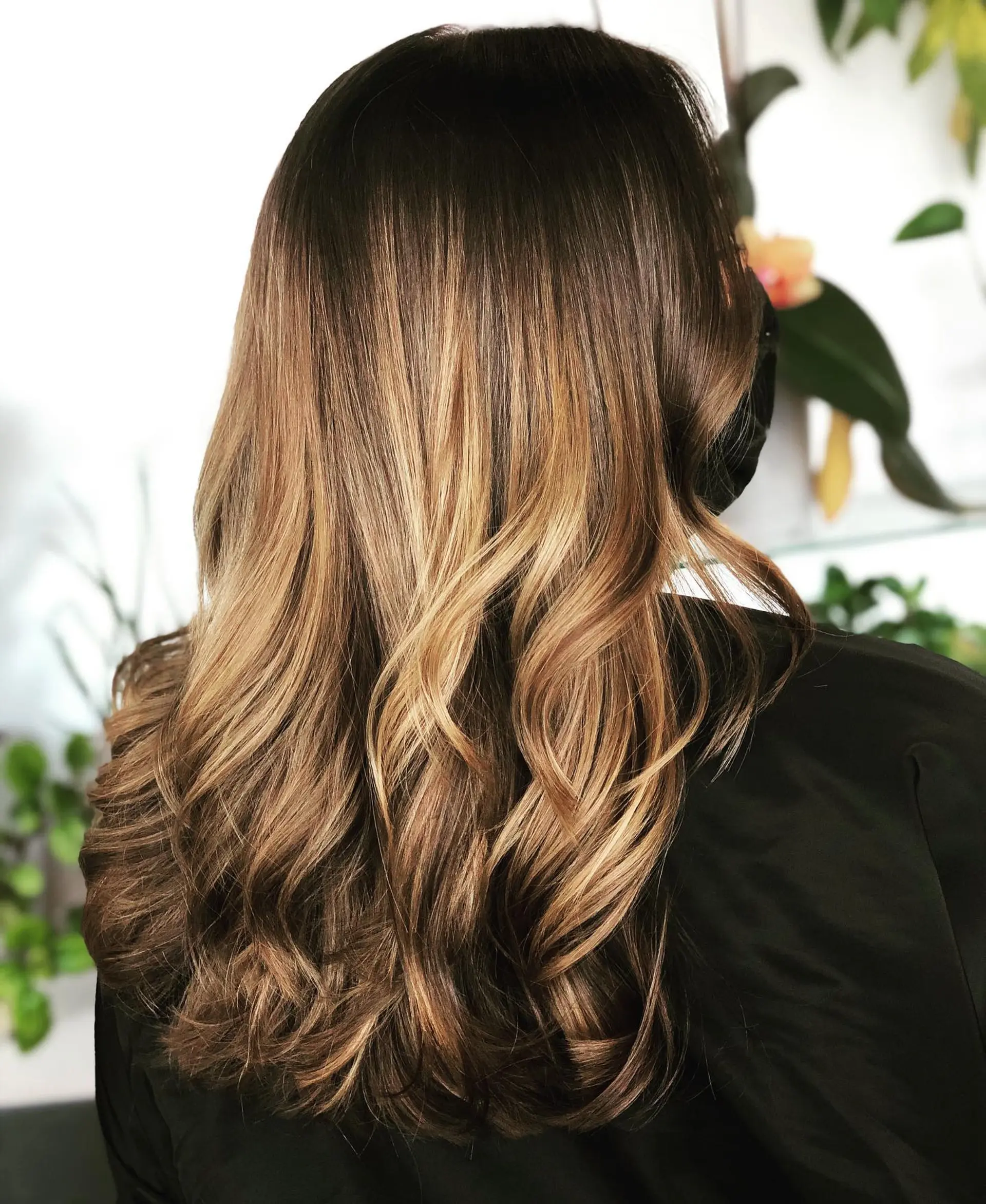 Long dimensional brunette hair with warm caramel balayage styled into voluminous, soft waves. 1