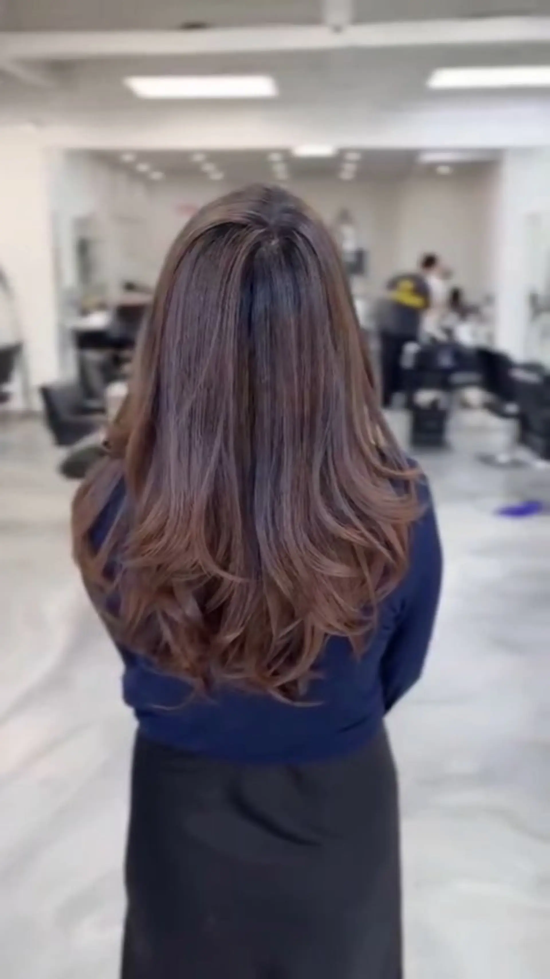 Long layered brunette hair with subtle cognac balayage highlights, styled into a voluminous blowout with soft outward-turned ends. 1