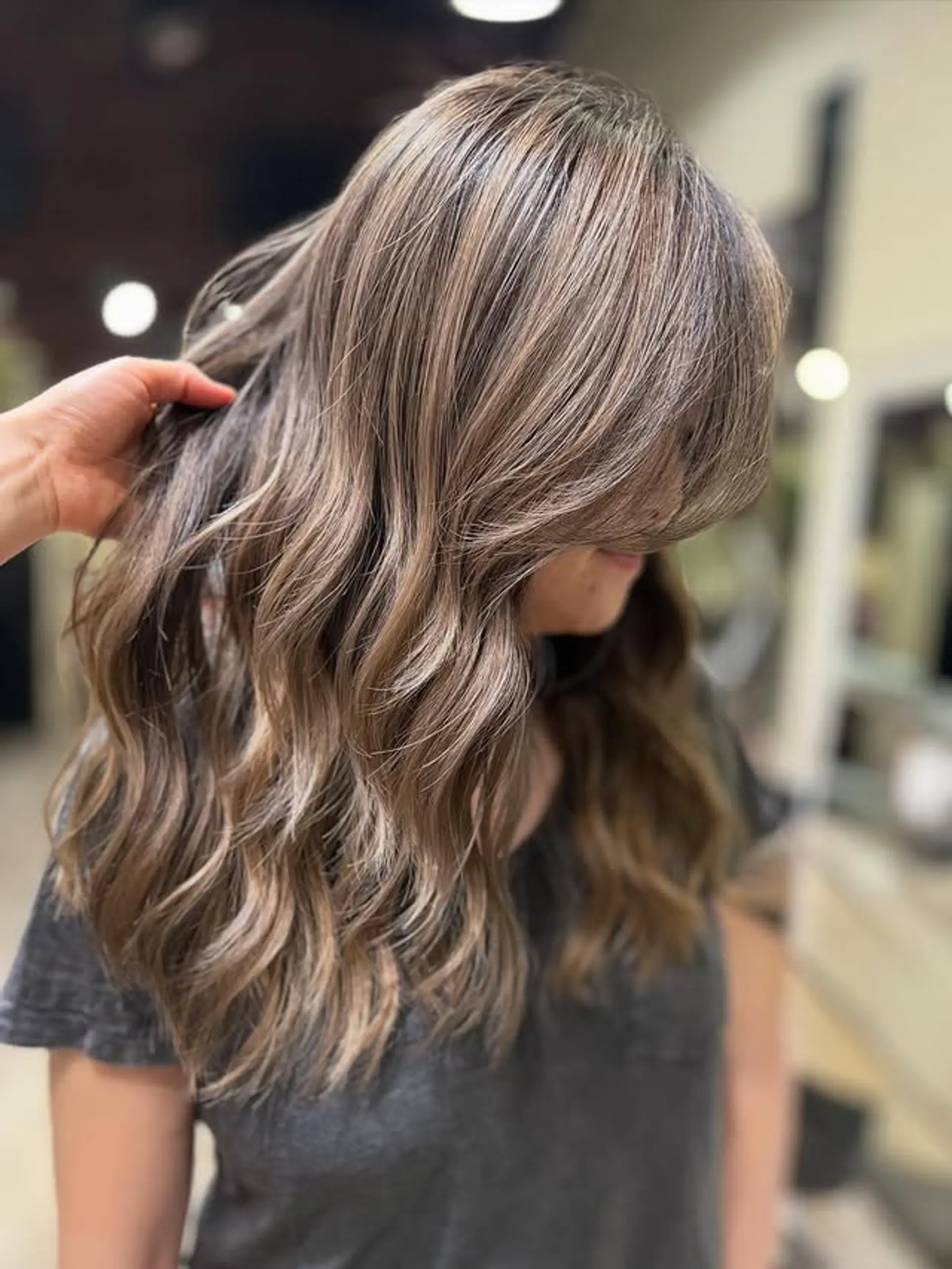 Long, flowing hair styled with soft, natural-looking waves and subtle layers that add movement and volume. The balayage technique creates a dimensional effect, blending lighter tones seamlessly into the darker base. 1
