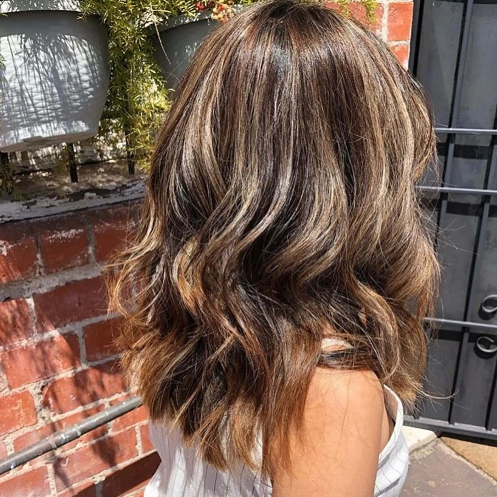 Medium-length dimensional brunette hair with warm caramel highlights, styled into loose textured waves. 1