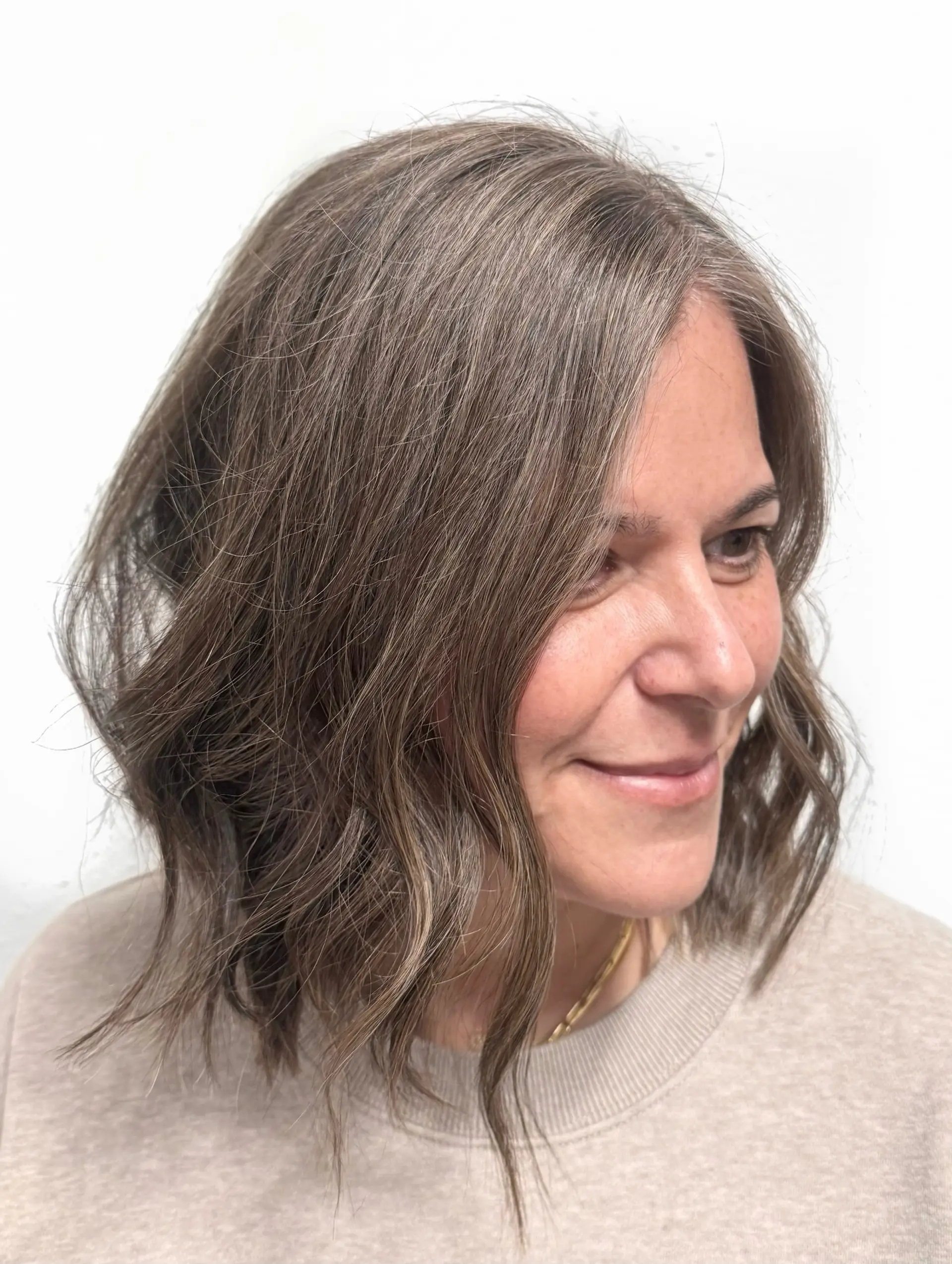 A textured shoulder-length wavy bob featuring soft babylights and seamless gray blending. 1