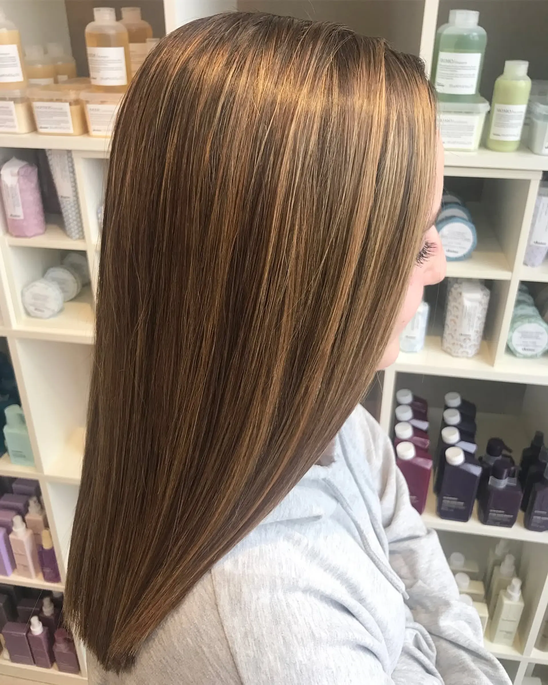 Long, glossy straight brunette hair featuring blended caramel balayage highlights. 1
