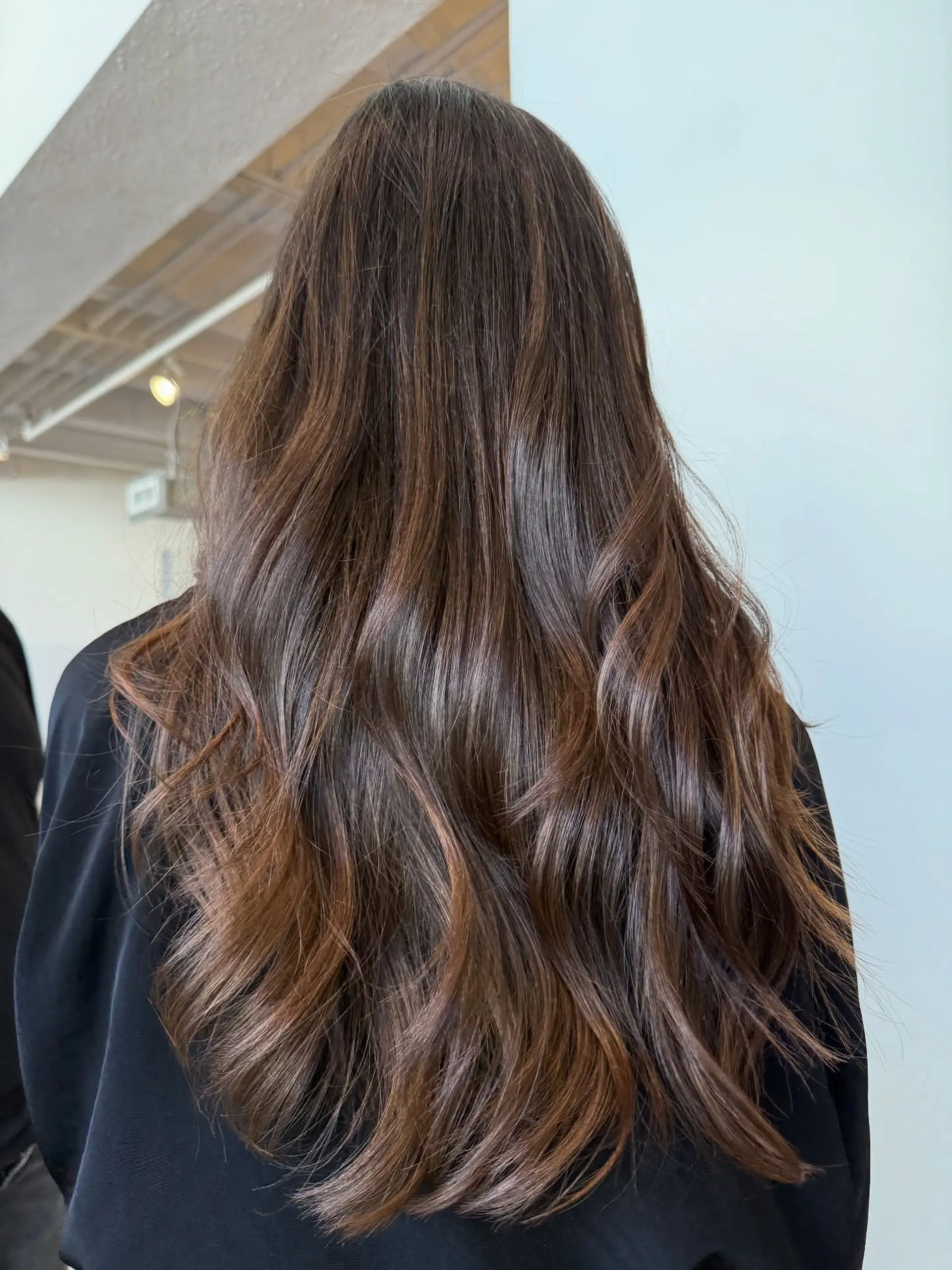 Long chocolate brown hair featuring delicate caramel and chestnut balayage highlights, styled in loose, textured waves. 1