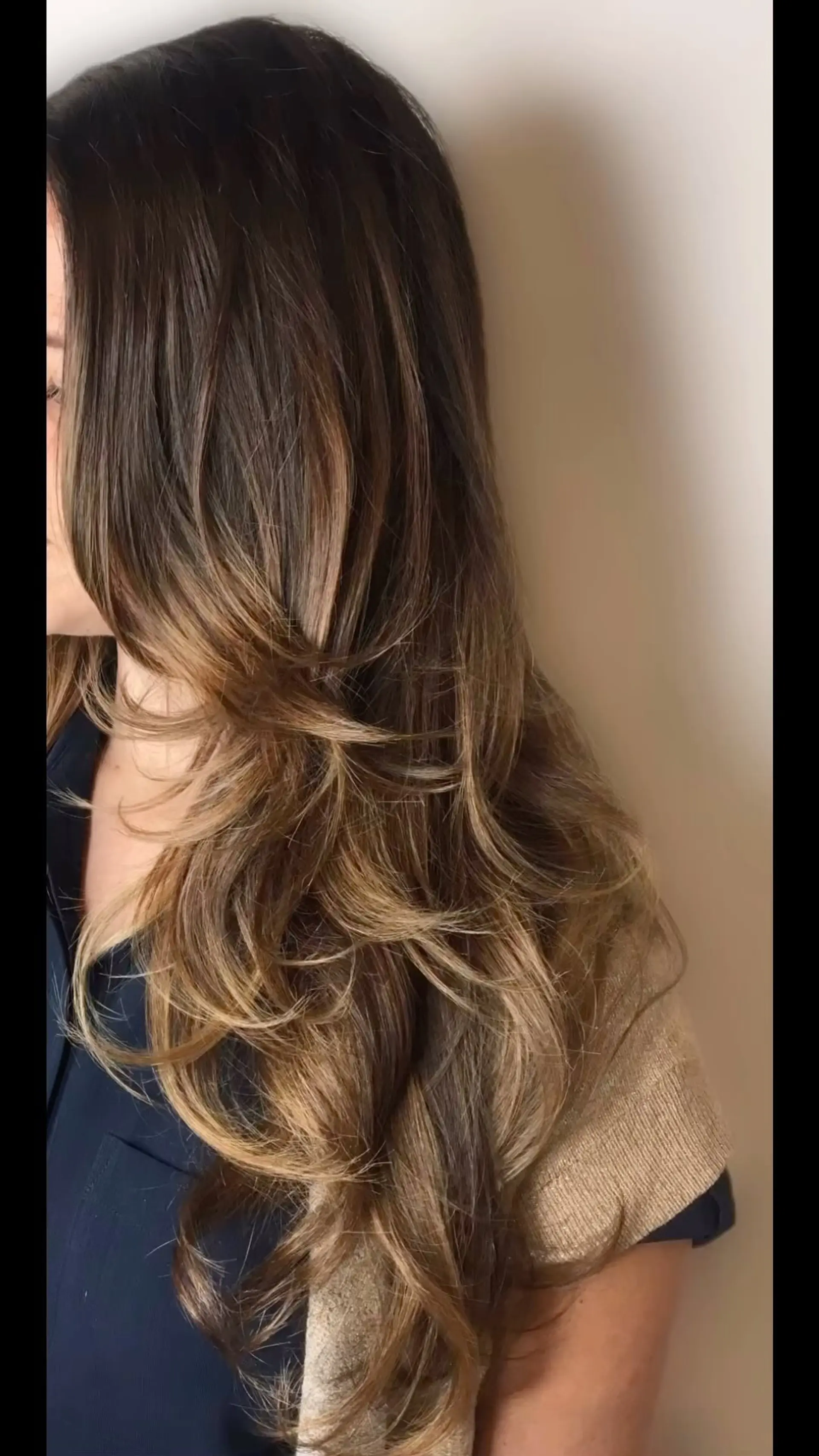 Long brunette hair styled in voluminous, layered waves with warm caramel and honey balayage highlights. 1