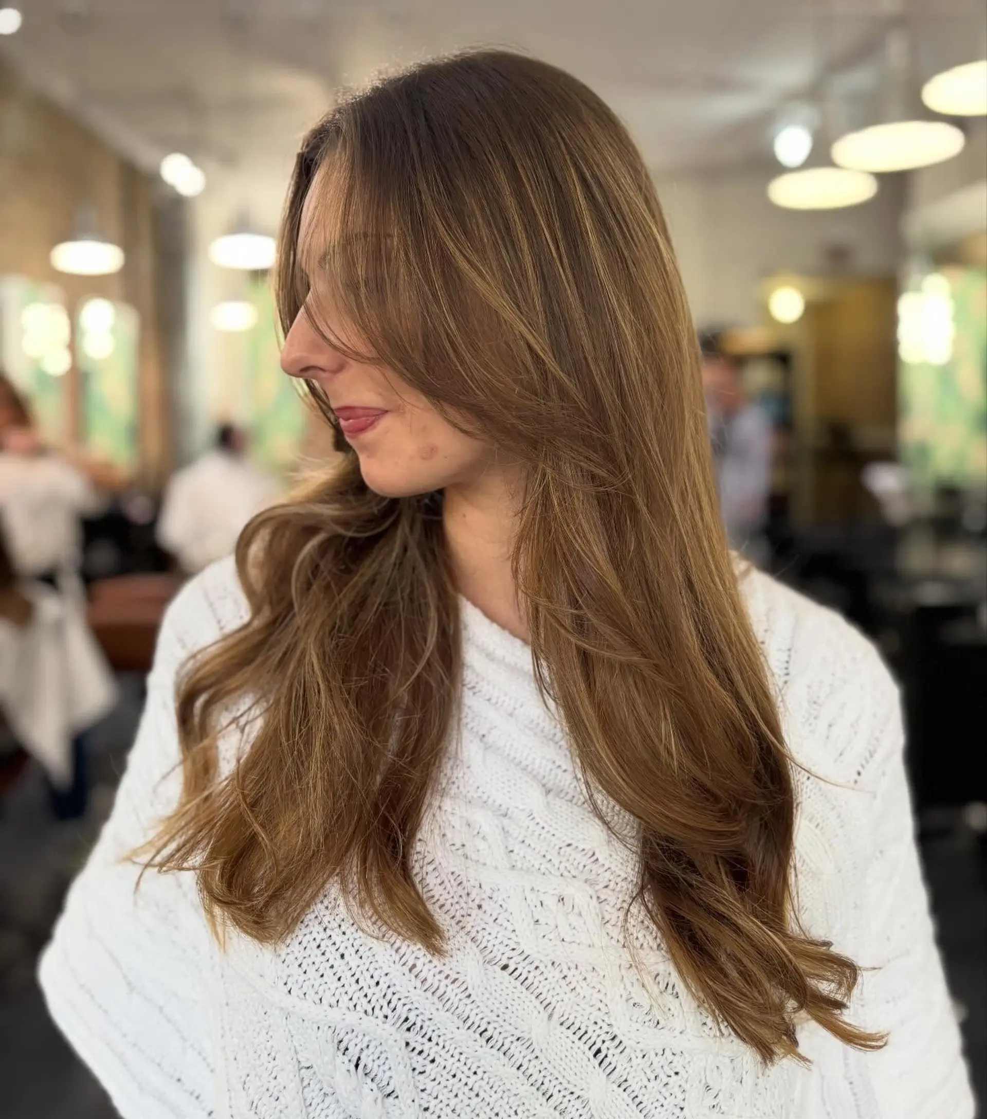 Long warm brunette hair with subtle sun-kissed highlights, face-framing layers, and soft blowout waves. 1