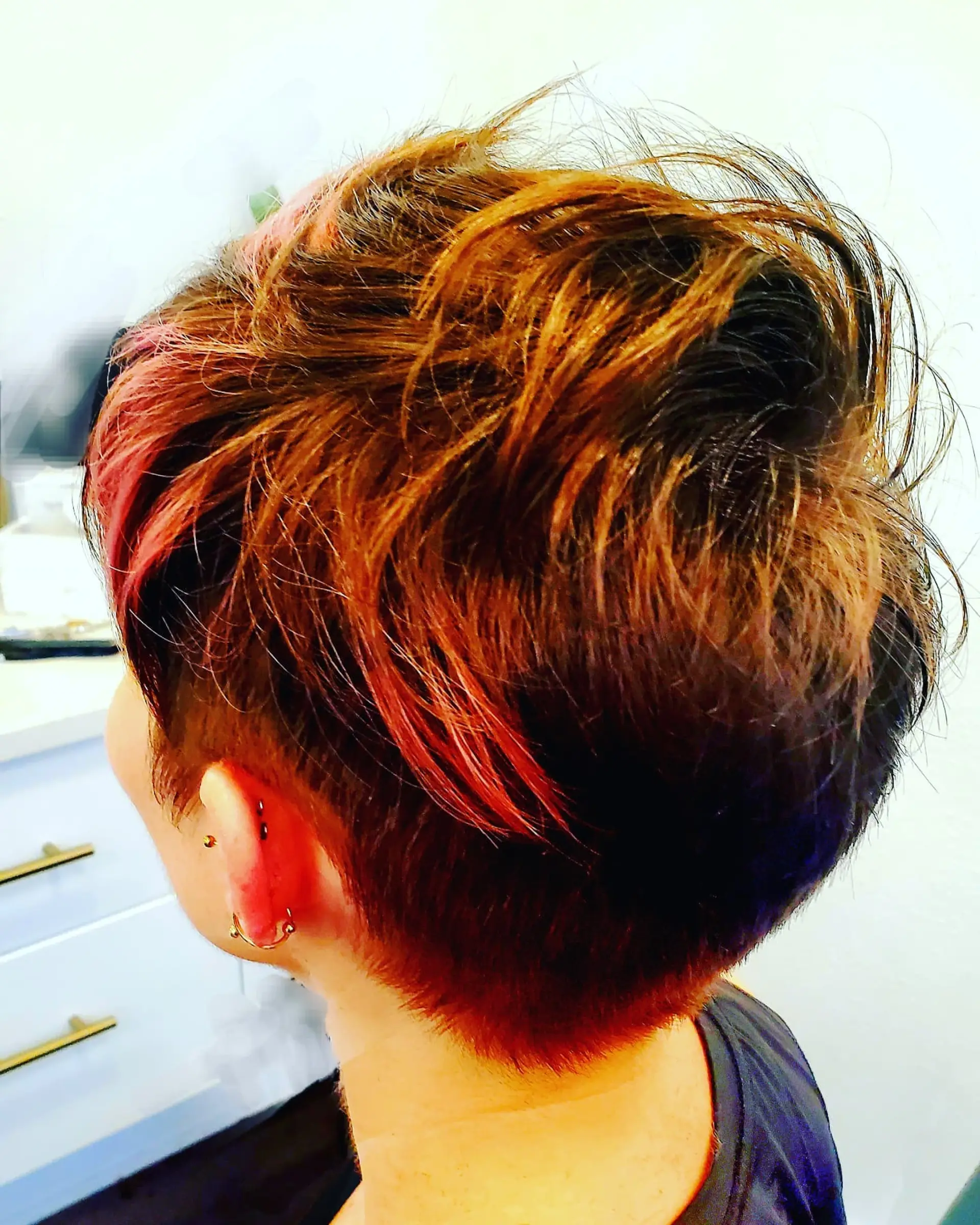 A textured short pixie cut featuring clipped sides and nape with longer crown layers, highlighted with vibrant pink and copper accents. 1