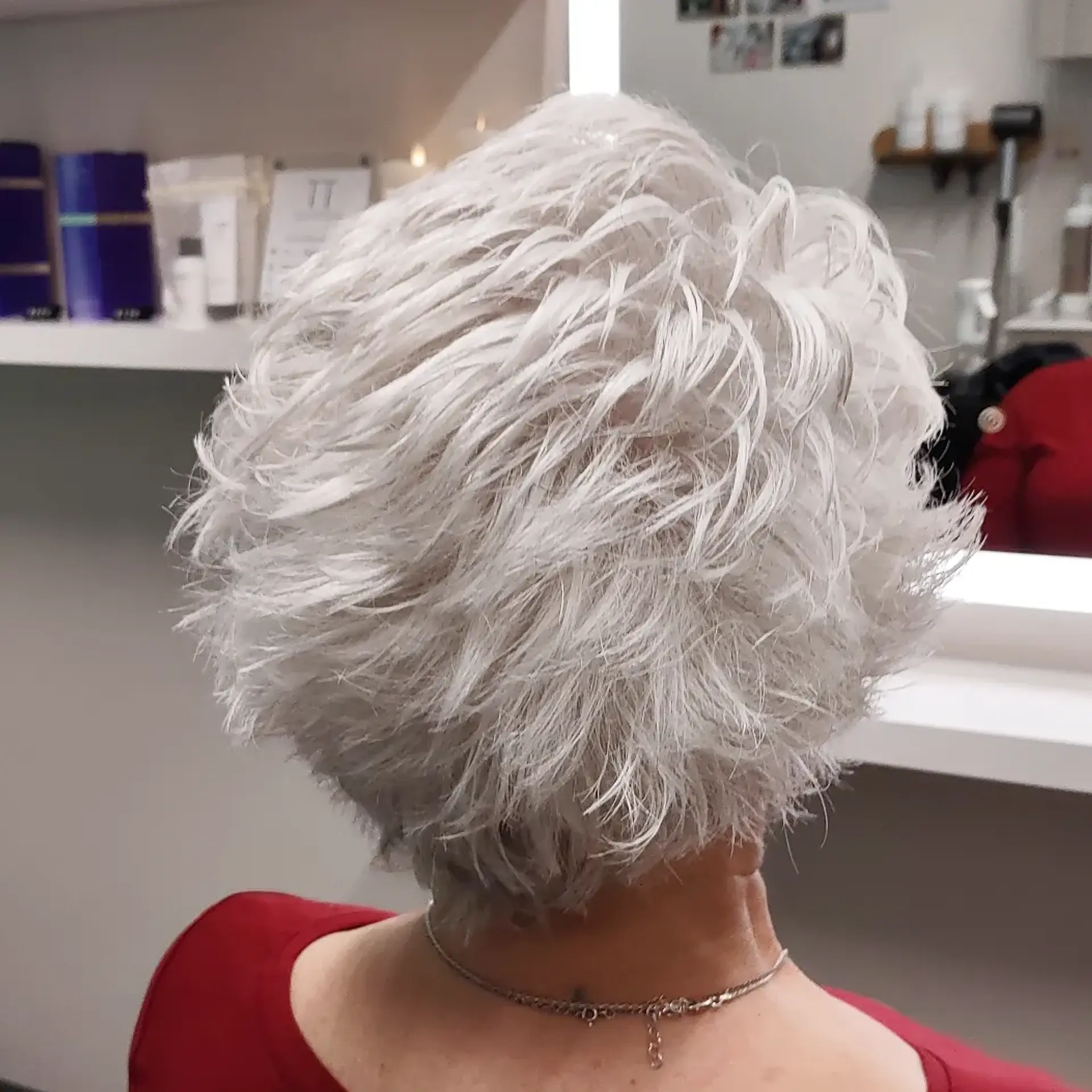 A short, heavily layered and textured pixie haircut styled with piecey volume in a radiant silver-white tone. 1
