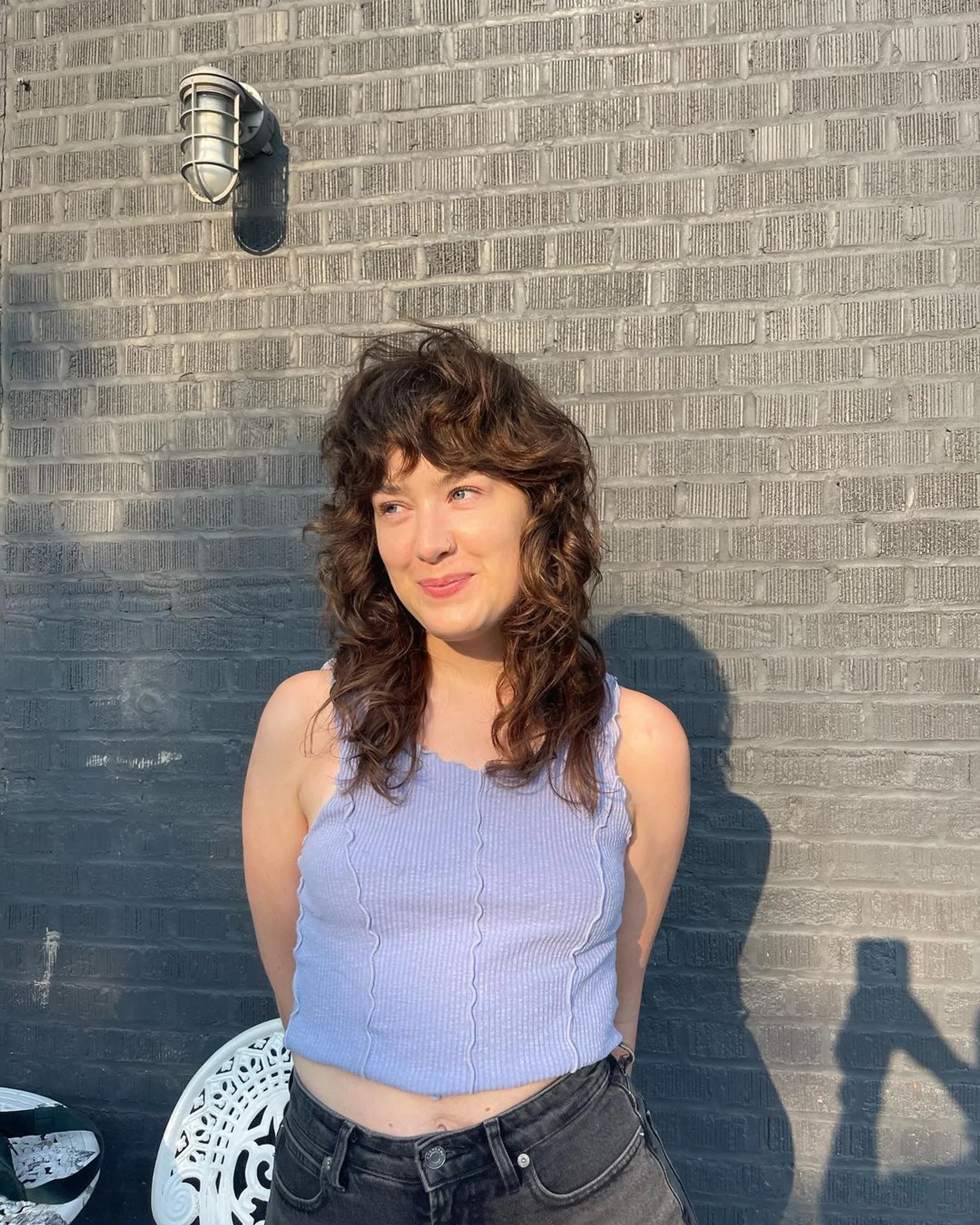 A woman with a modern, medium-length retro shag haircut with face-framing curtain bangs and sun-kissed blonde highlights. - Preview 2