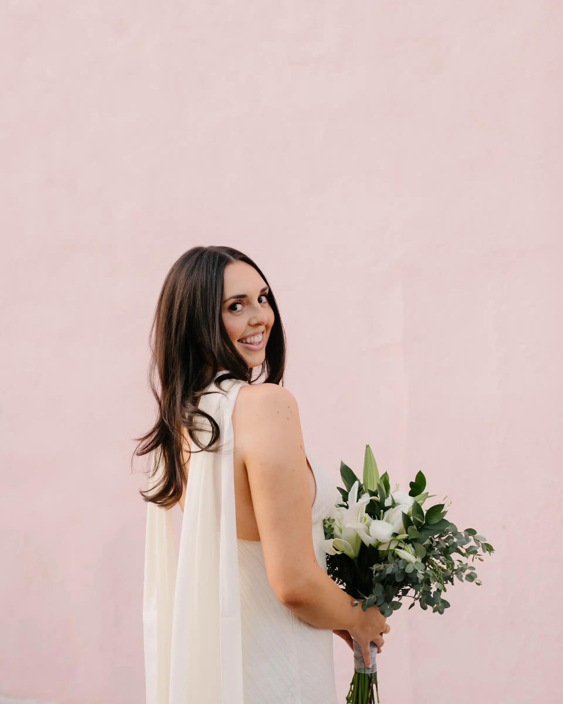 A sleek and romantic bridal downstyle featuring healthy, dark brown hair with smooth texture and soft, flipped-out curled ends. 1