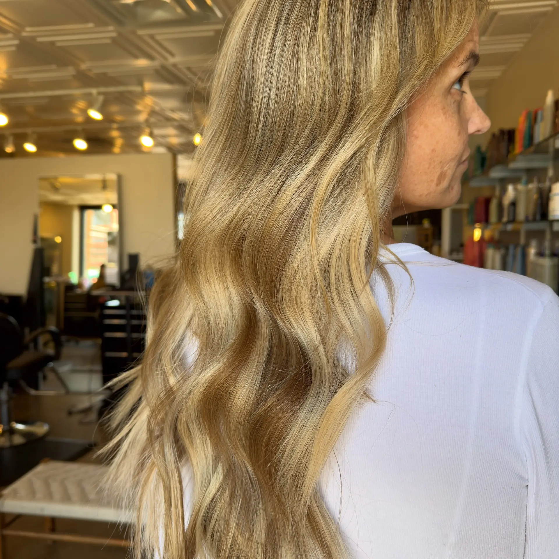 Long warm golden blonde hair with seamless extensions styled into loose, gentle waves. 1