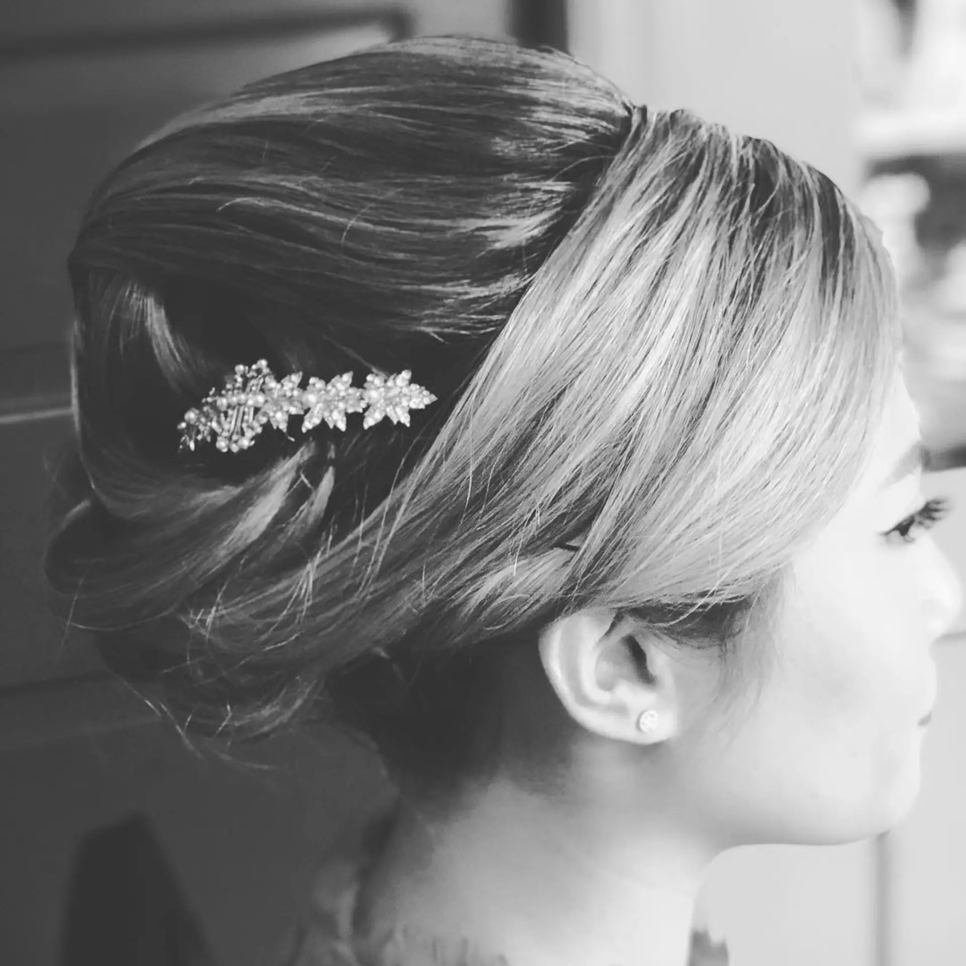 A sophisticated formal updo styled with a smooth, voluminous crown and pinned into an elegant twist accented with a crystal clip. 1