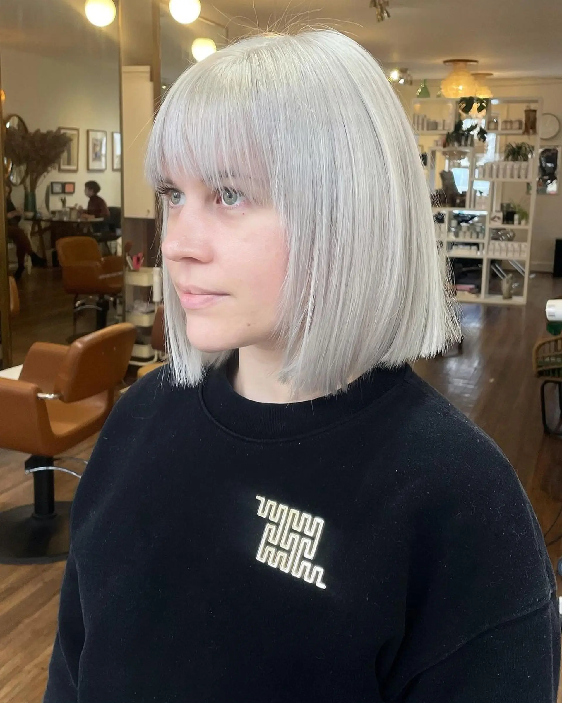 A sleek medium-length bob with a blunt cut and straight fringe in platinum silver, featuring a polished and shiny finish. 1
