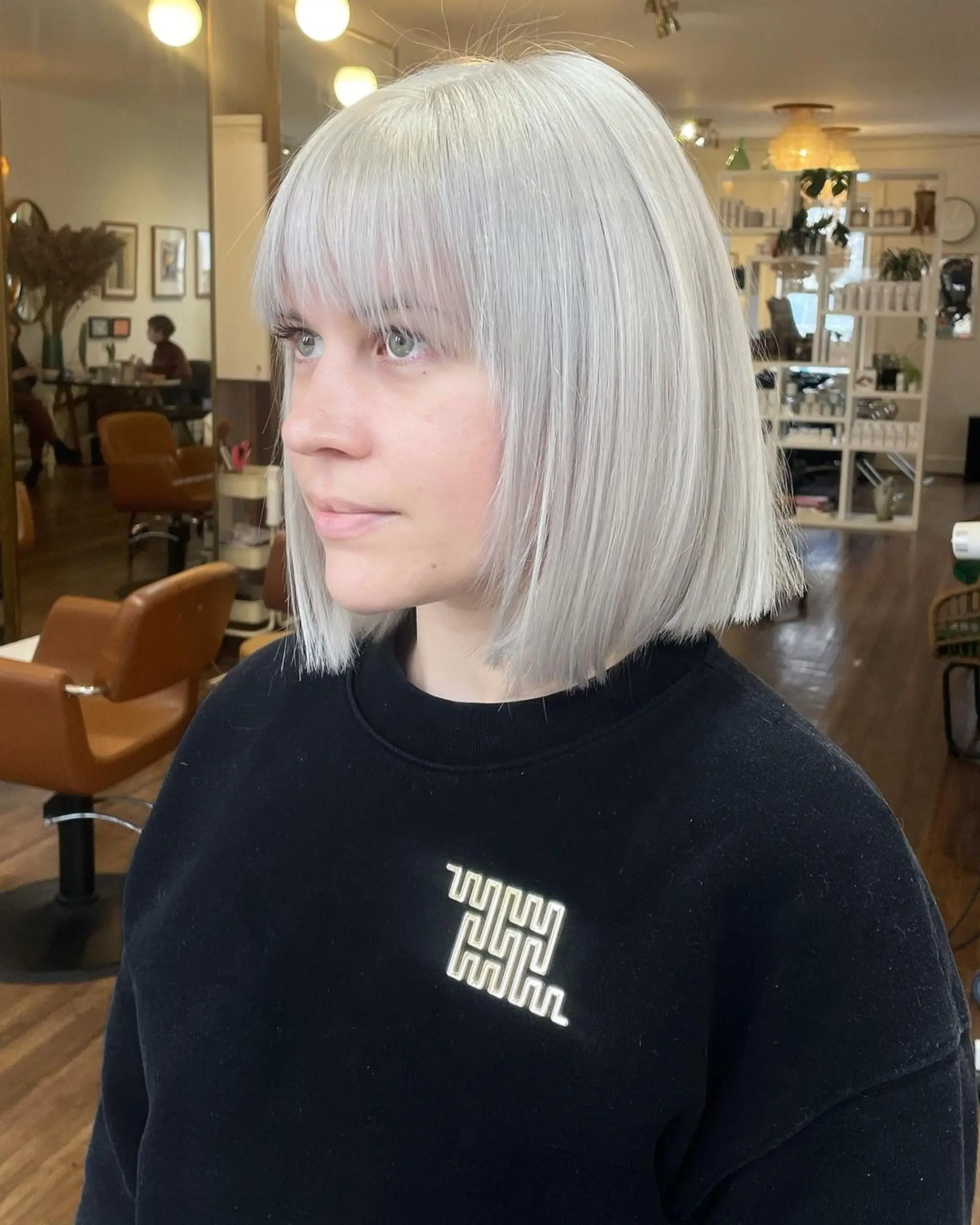 A sleek medium-length bob with a blunt cut and straight fringe in platinum silver, featuring a polished and shiny finish.