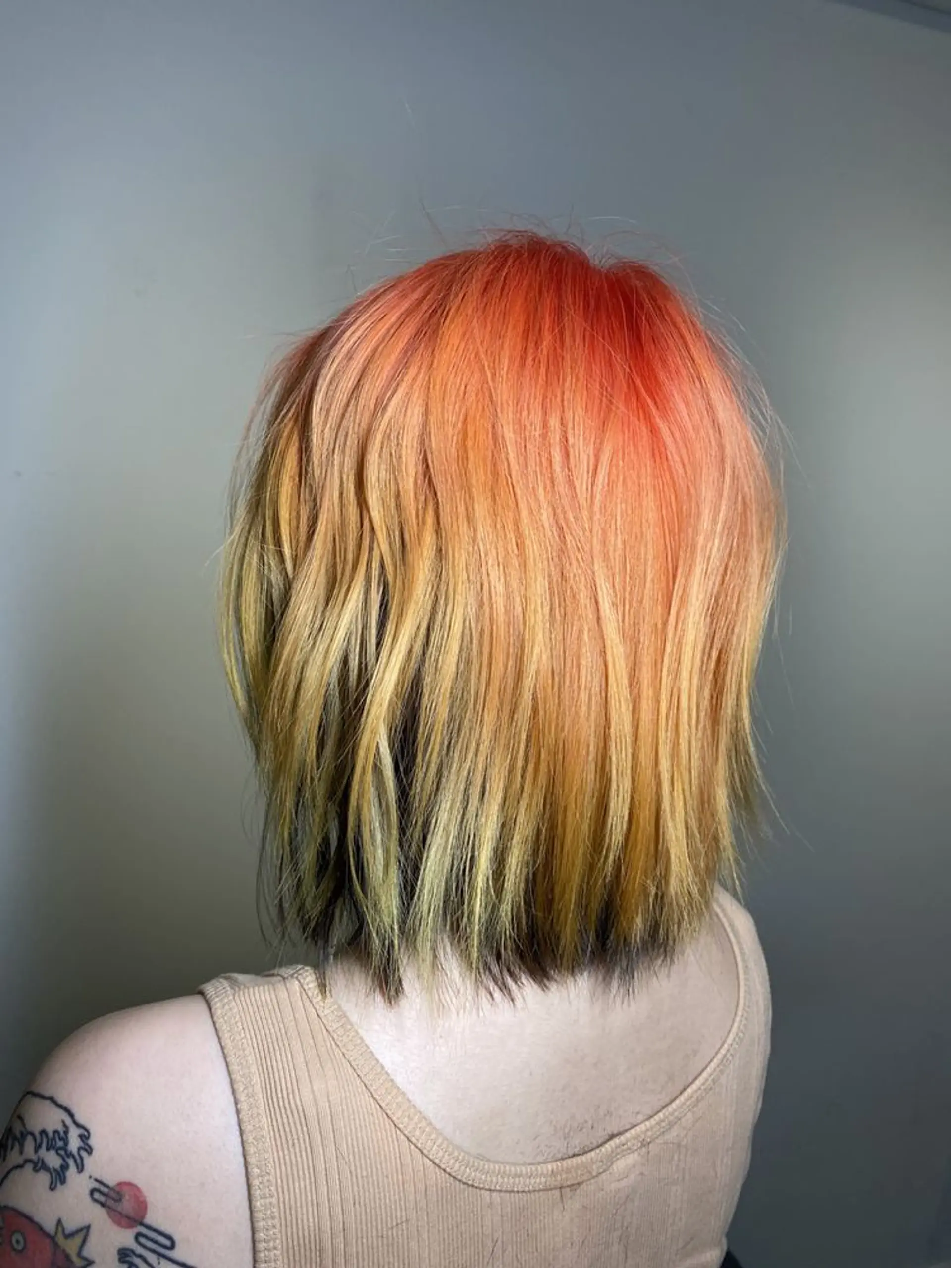 A wavy, short bob with an ombre effect featuring fiery orange roots transitioning to yellow and blonde ends, styled with loose waves. 2