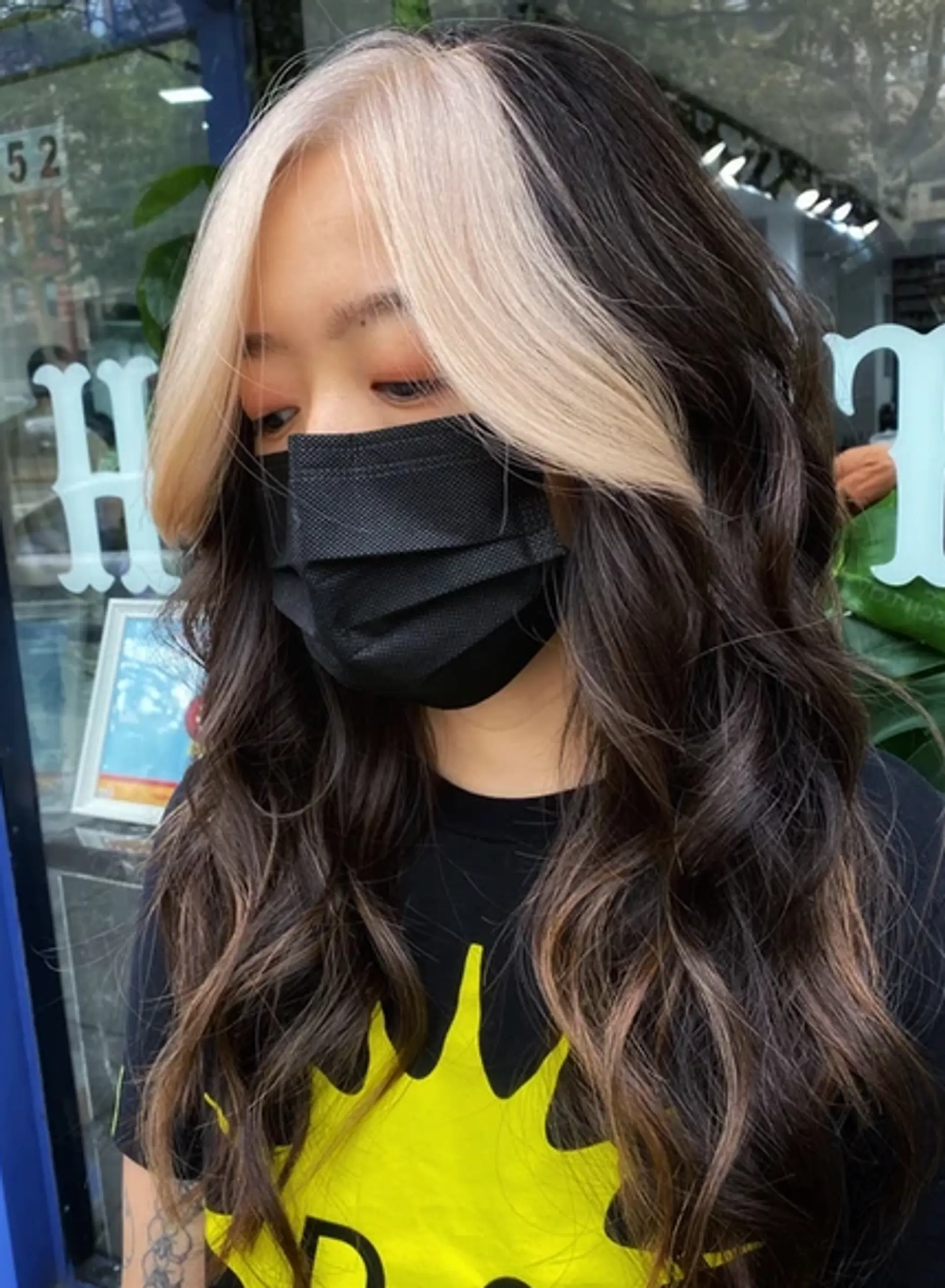Long, wavy black hair with a striking platinum blonde face-framing streak that starts from the roots and flows down. Voluminous and relaxed waves add texture and movement. 1
