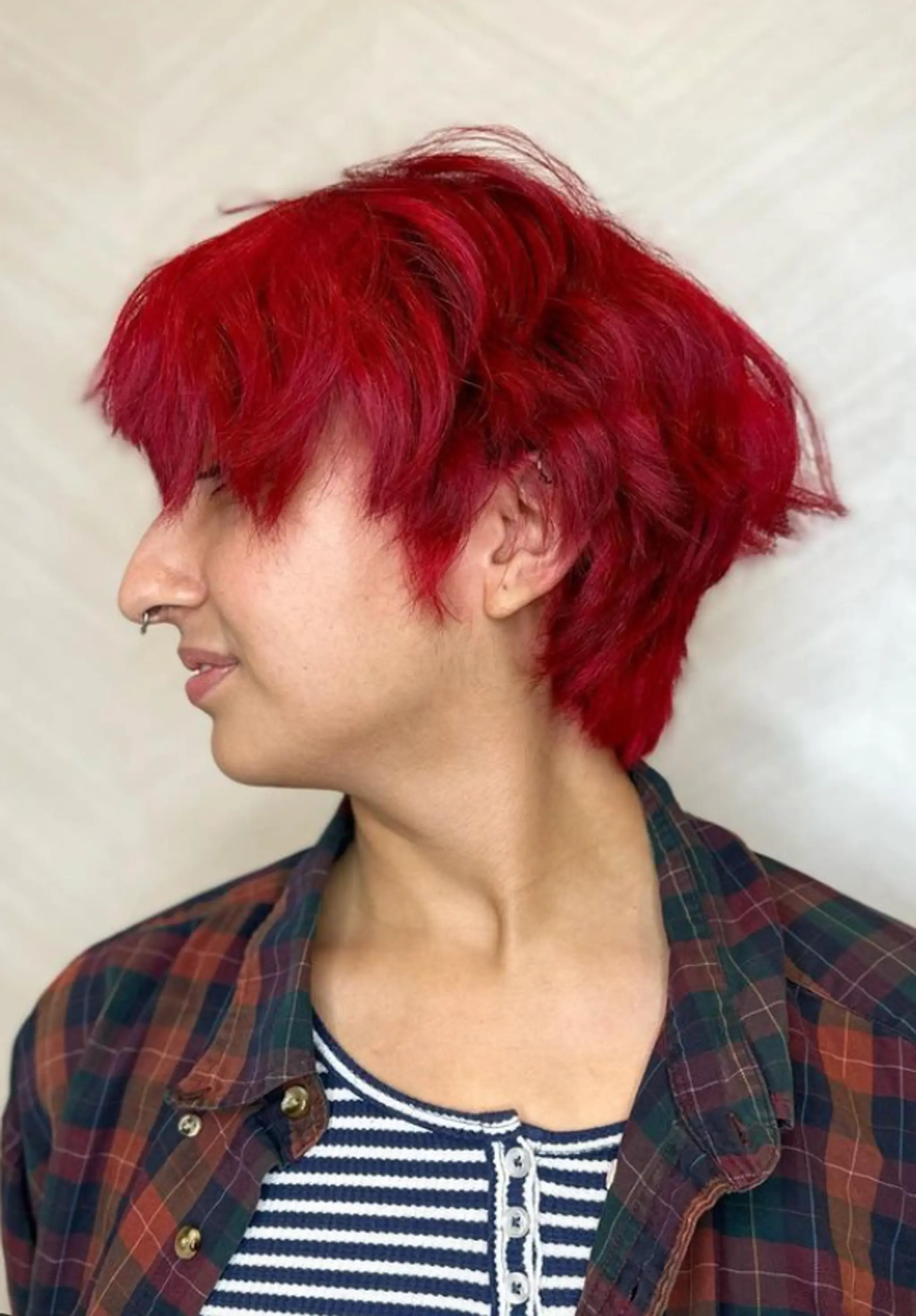 A daring and vibrant short hairstyle with a striking red color, wavy texture, messy layers, and an asymmetrical fringe. The tousled look adds a carefree and bold essence.