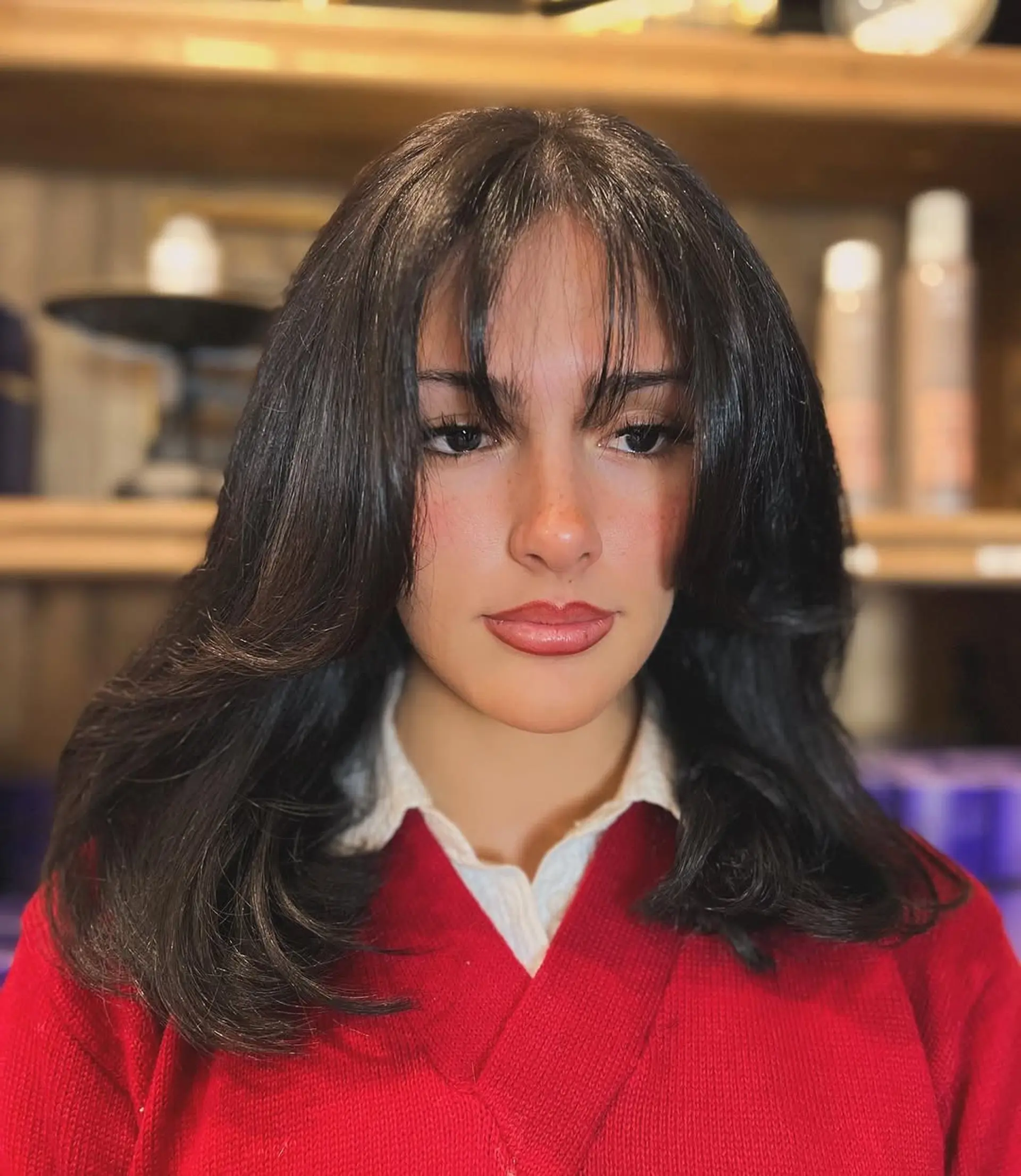 Medium-length wavy black hair with voluminous curtain bangs and face-framing layers, featuring a glossy, elegant finish. 1