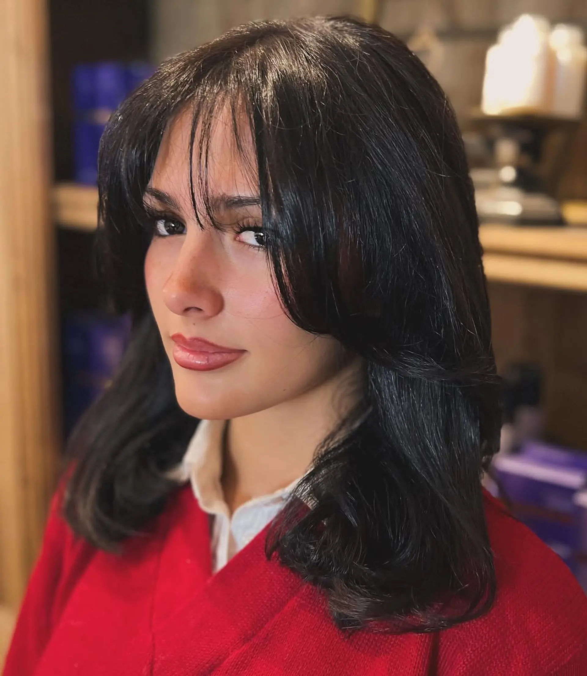 Medium-length wavy black hair with voluminous curtain bangs and face-framing layers, featuring a glossy, elegant finish. 2