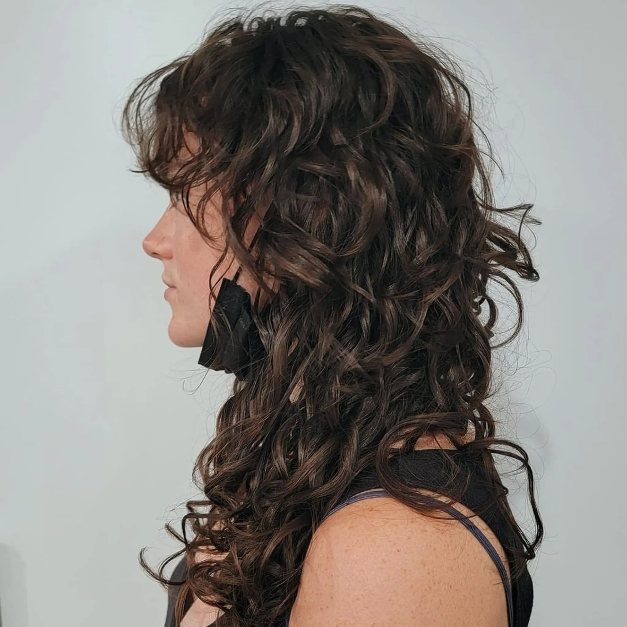 Long, dark brown curly hair with well-defined curls, voluminous layers, and a side part, creating a lively and dynamic appearance.