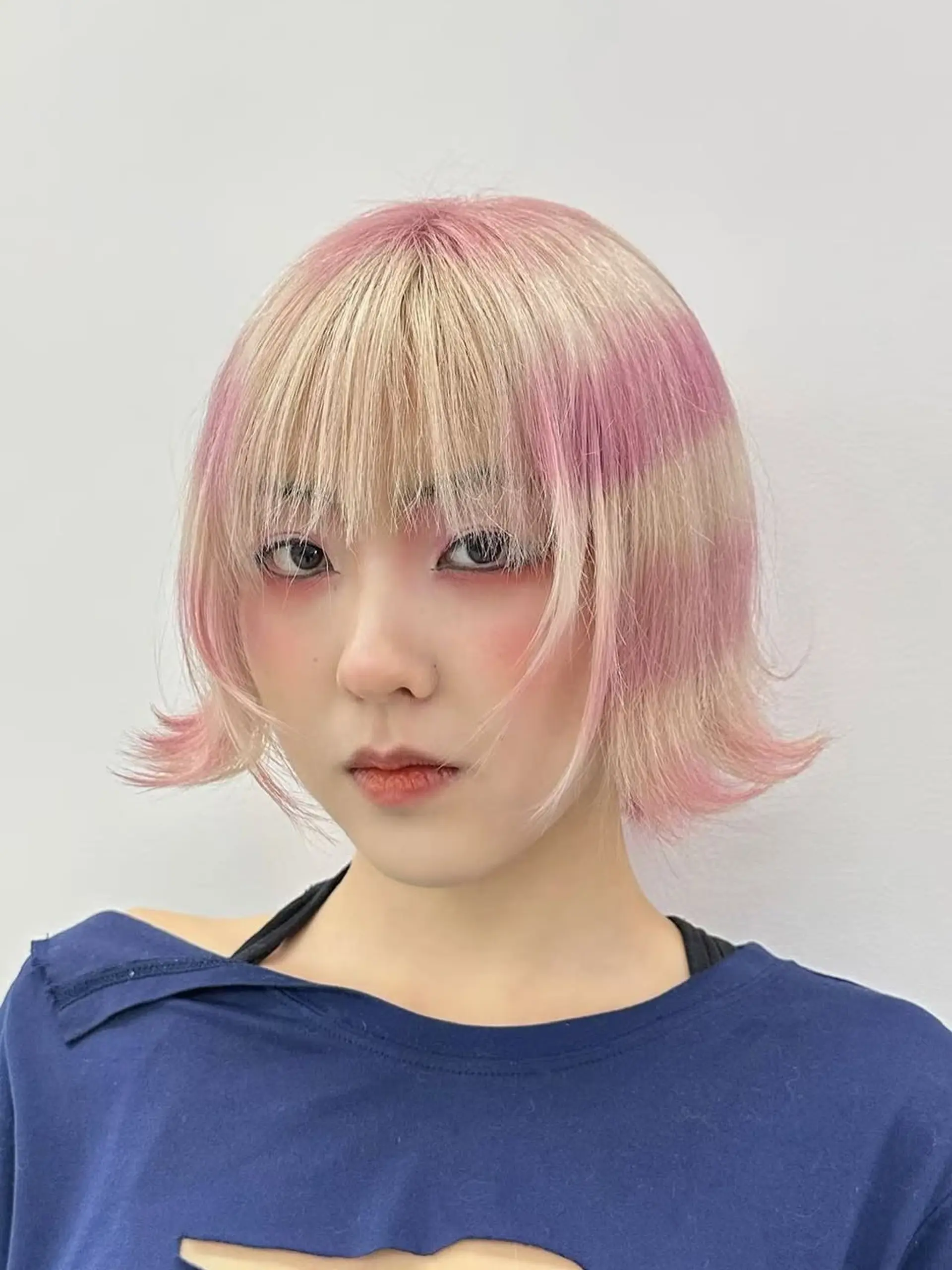 A layered chin-length bob with wispy see-through bangs, styled with playful flared ends and a bold, two-tone block-coloring technique. 1