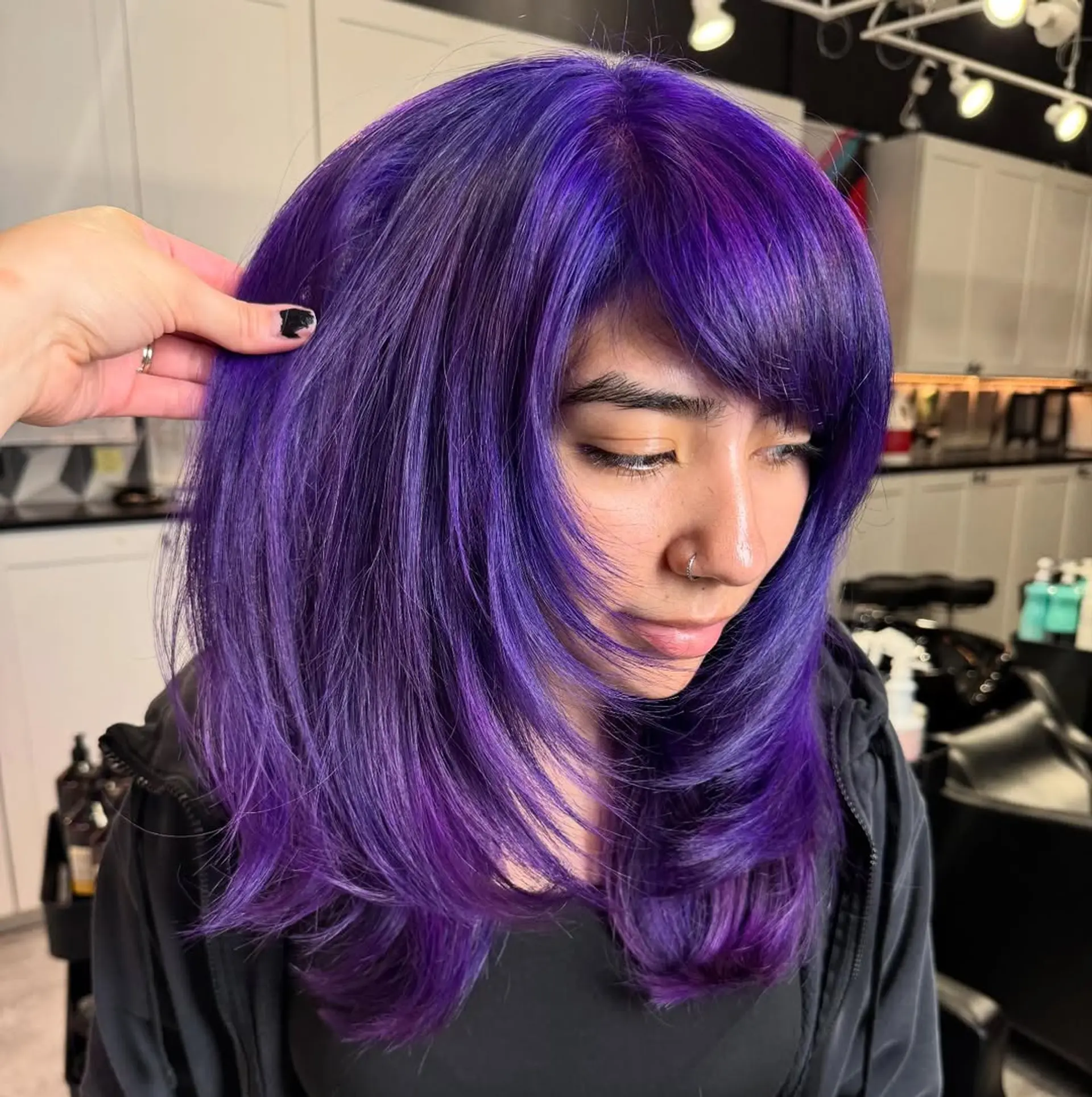 A stunning vibrant purple mid-length layered haircut featuring soft, face-framing bangs and feathered ends, creating a dynamic and playful silhouette. 1