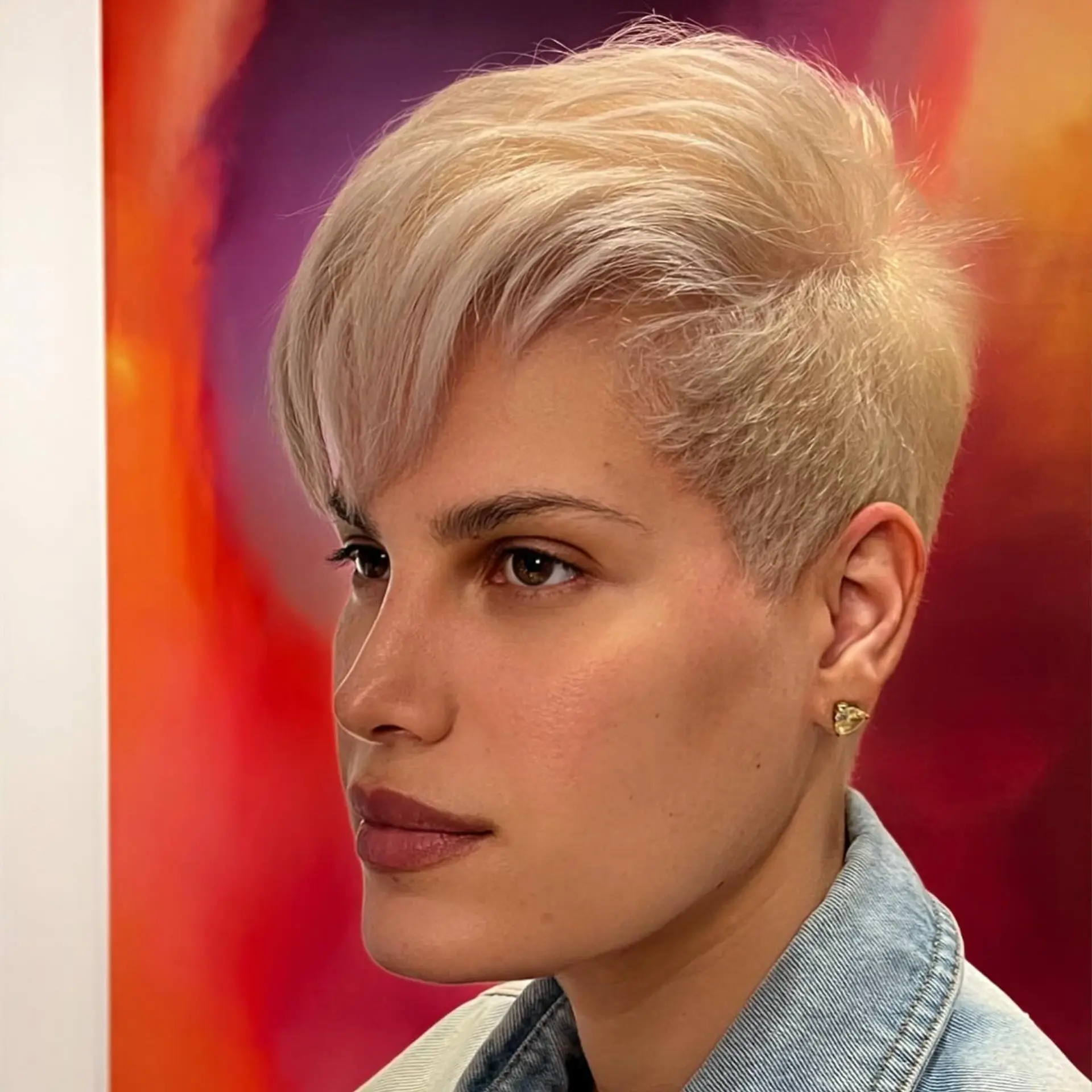 A textured platinum blonde pixie cut with closely tapered sides and a soft, side-swept fringe. 1