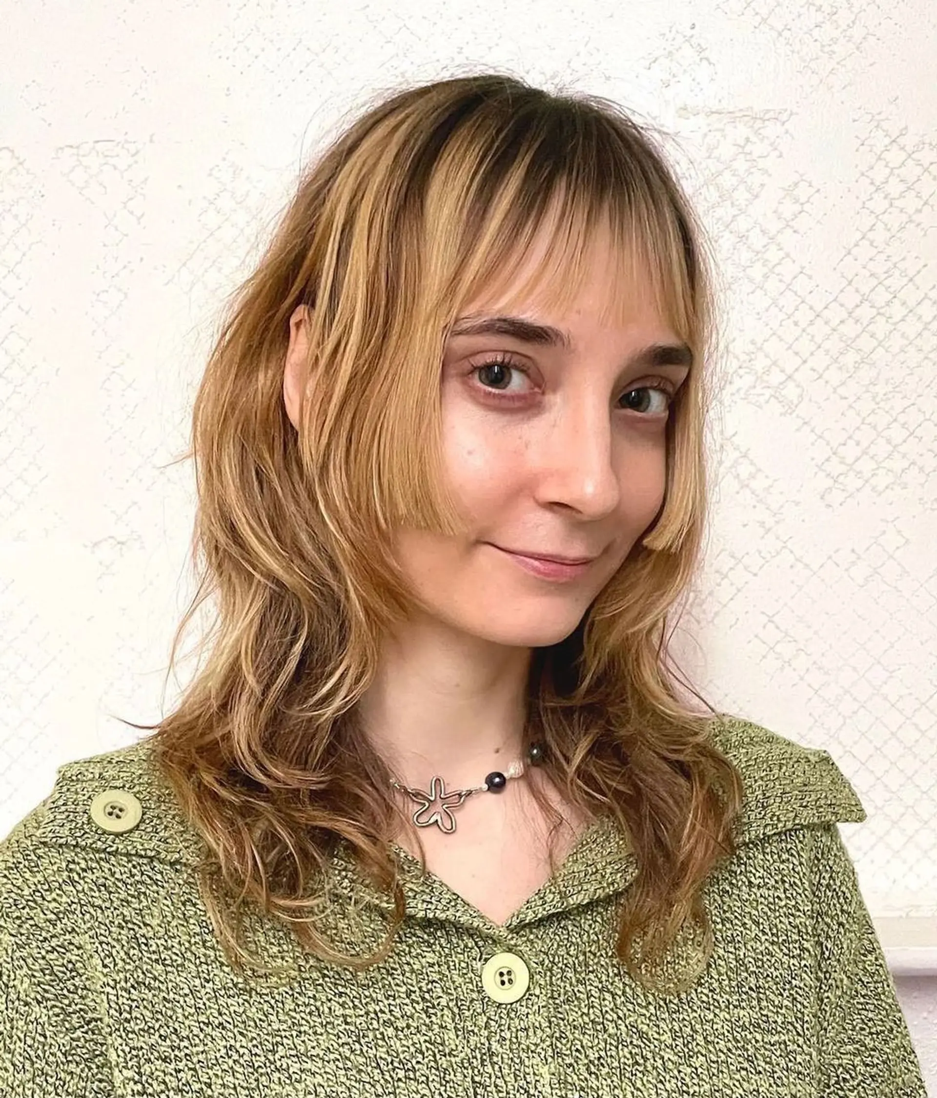 Medium-length wavy hairstyle with layered cuts and fringe bangs, highlighted with blonde and golden shades, offering a textured and radiant look. 1
