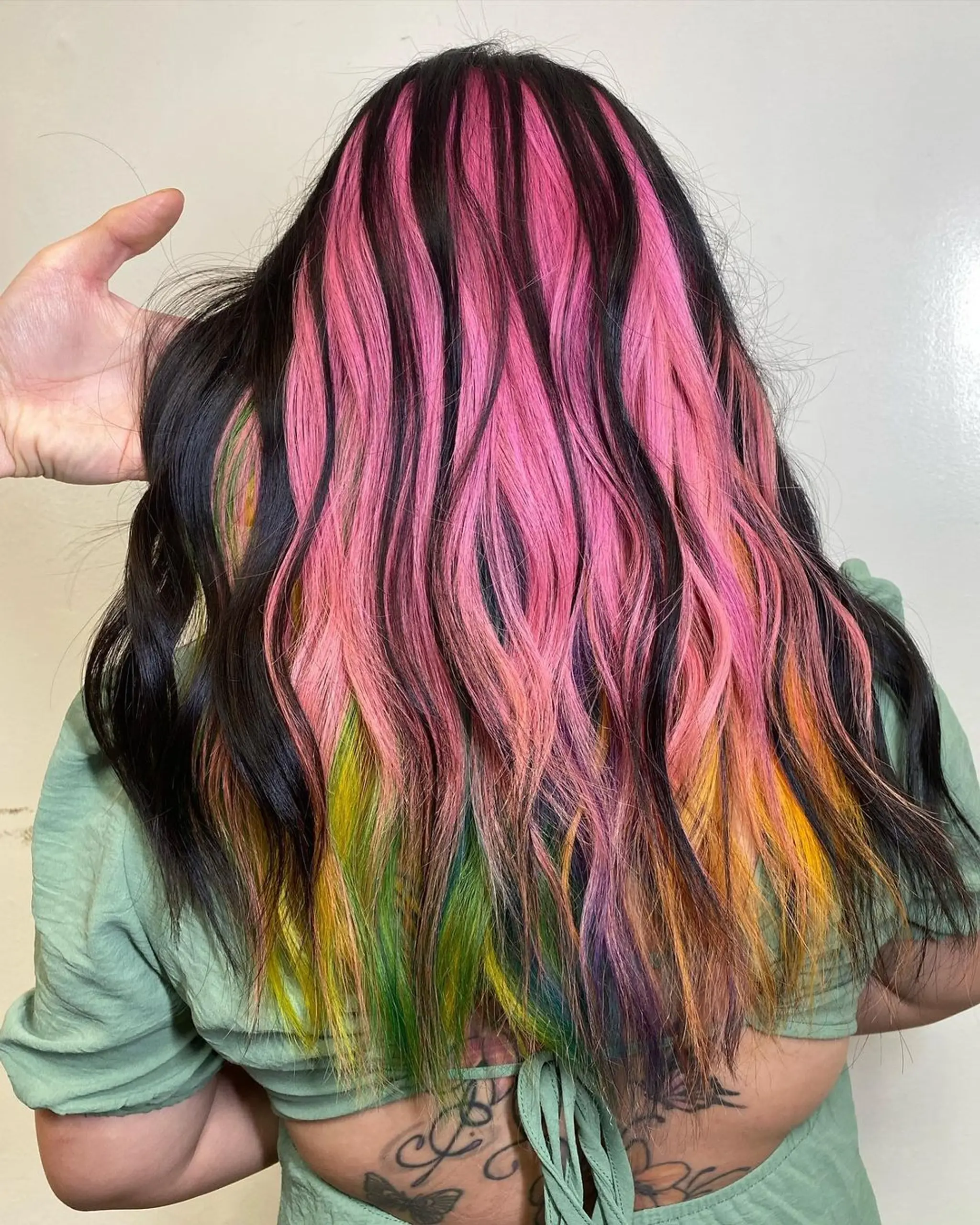 An intricate peekaboo hairstyle featuring medium-length wavy hair in black, yellow, green, purple, pink, and orange hues, parted at the crown and blending seamlessly into one another. 2
