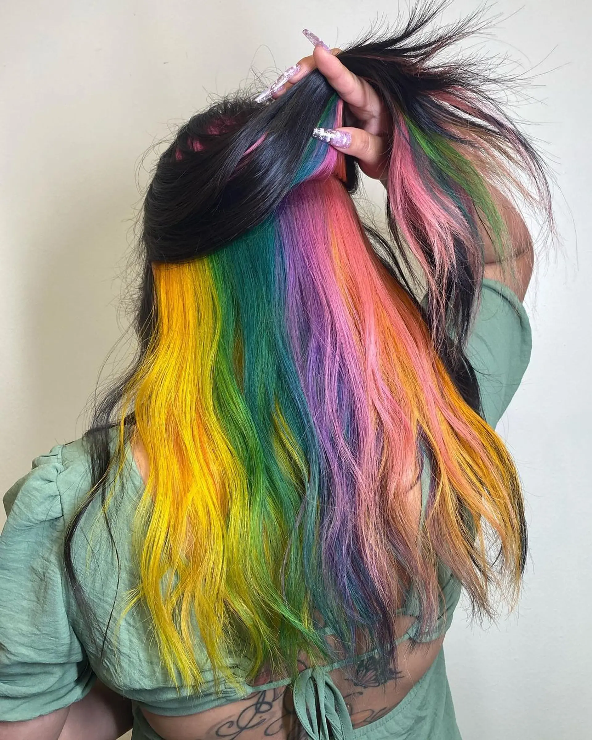 An intricate peekaboo hairstyle featuring medium-length wavy hair in black, yellow, green, purple, pink, and orange hues, parted at the crown and blending seamlessly into one another. 1