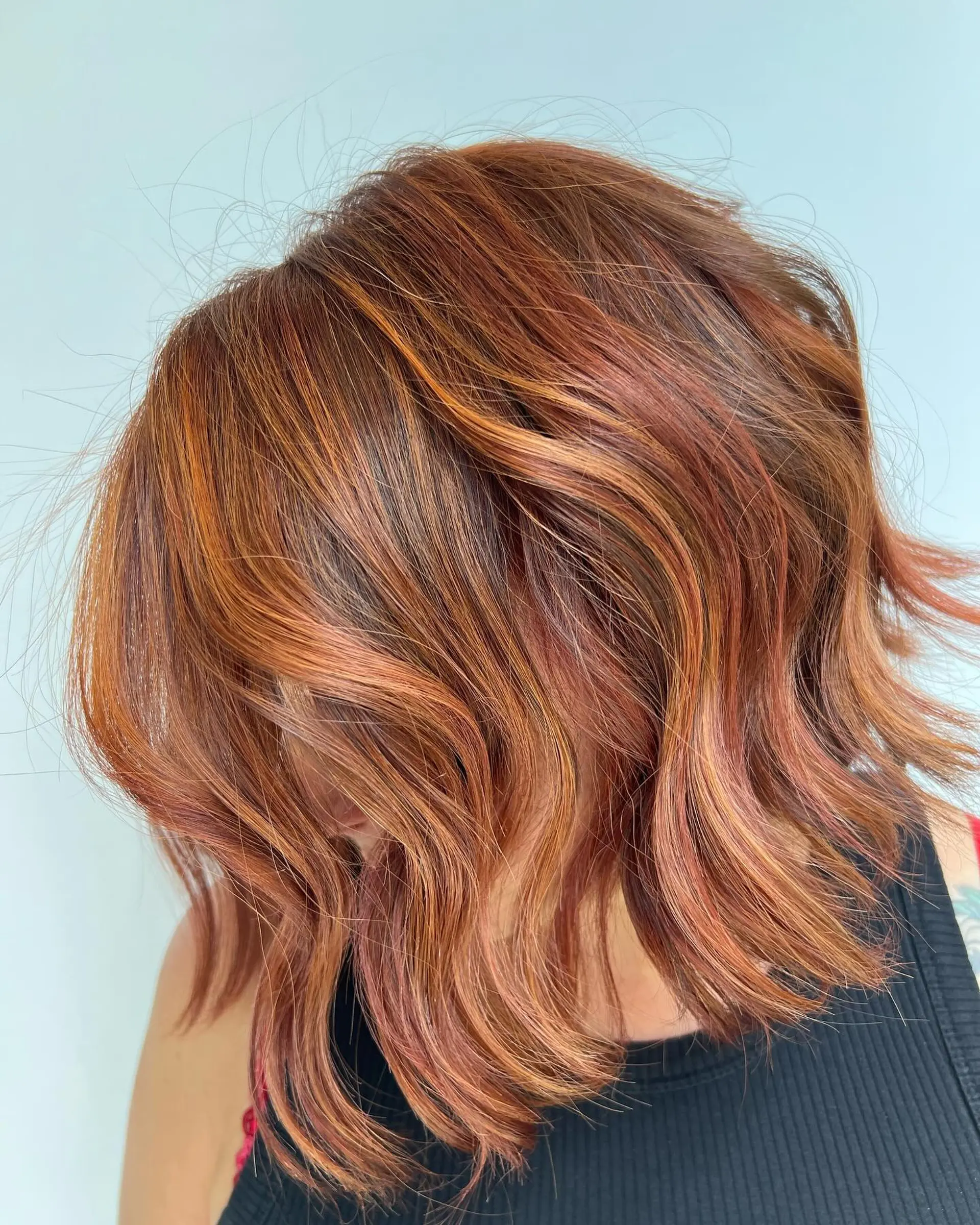 A textured shoulder-length bob styled in soft, undone waves with dimensional copper and auburn ribbon highlights. 1