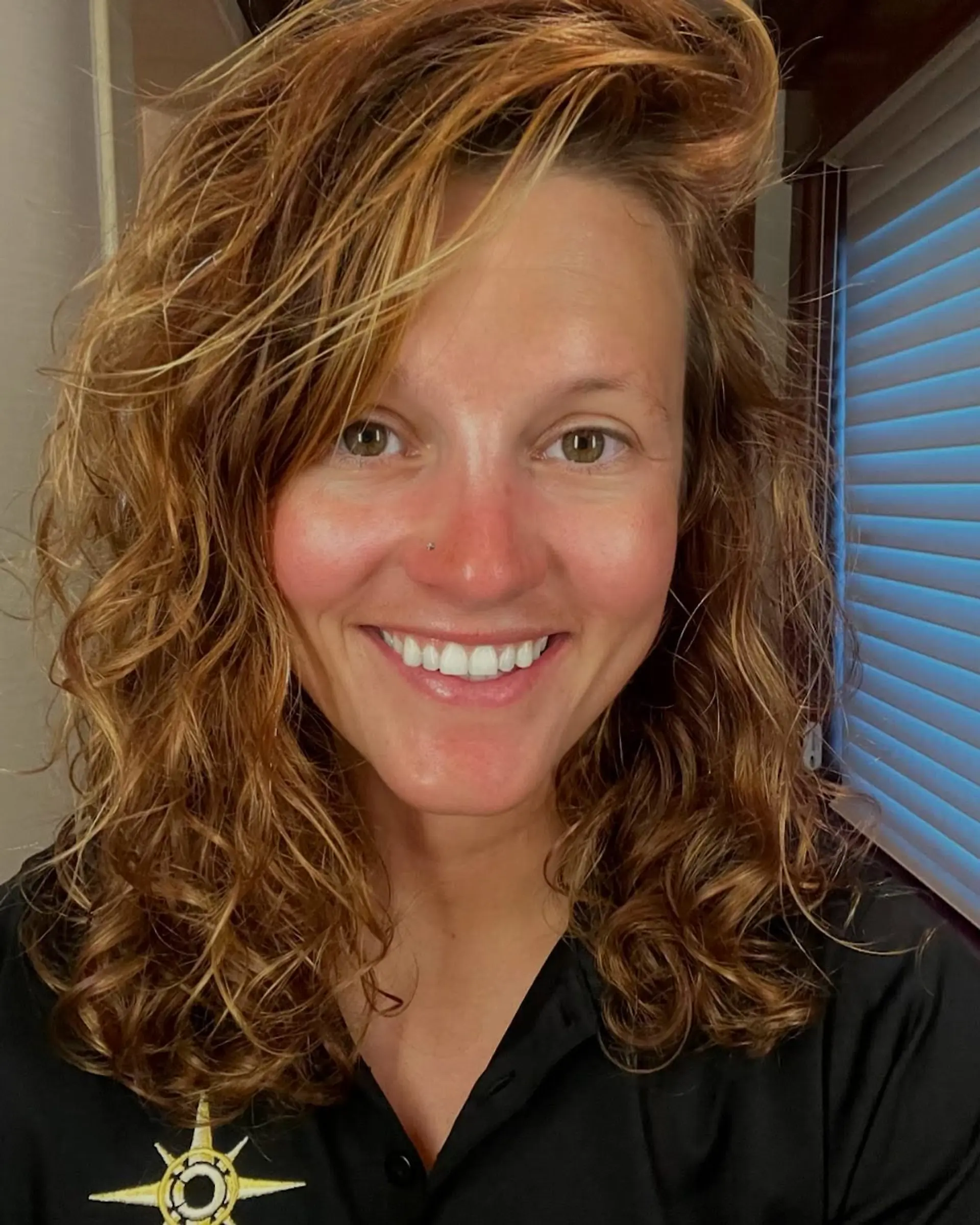 A curly, medium-length hairstyle with a dimensional blonde balayage. 1