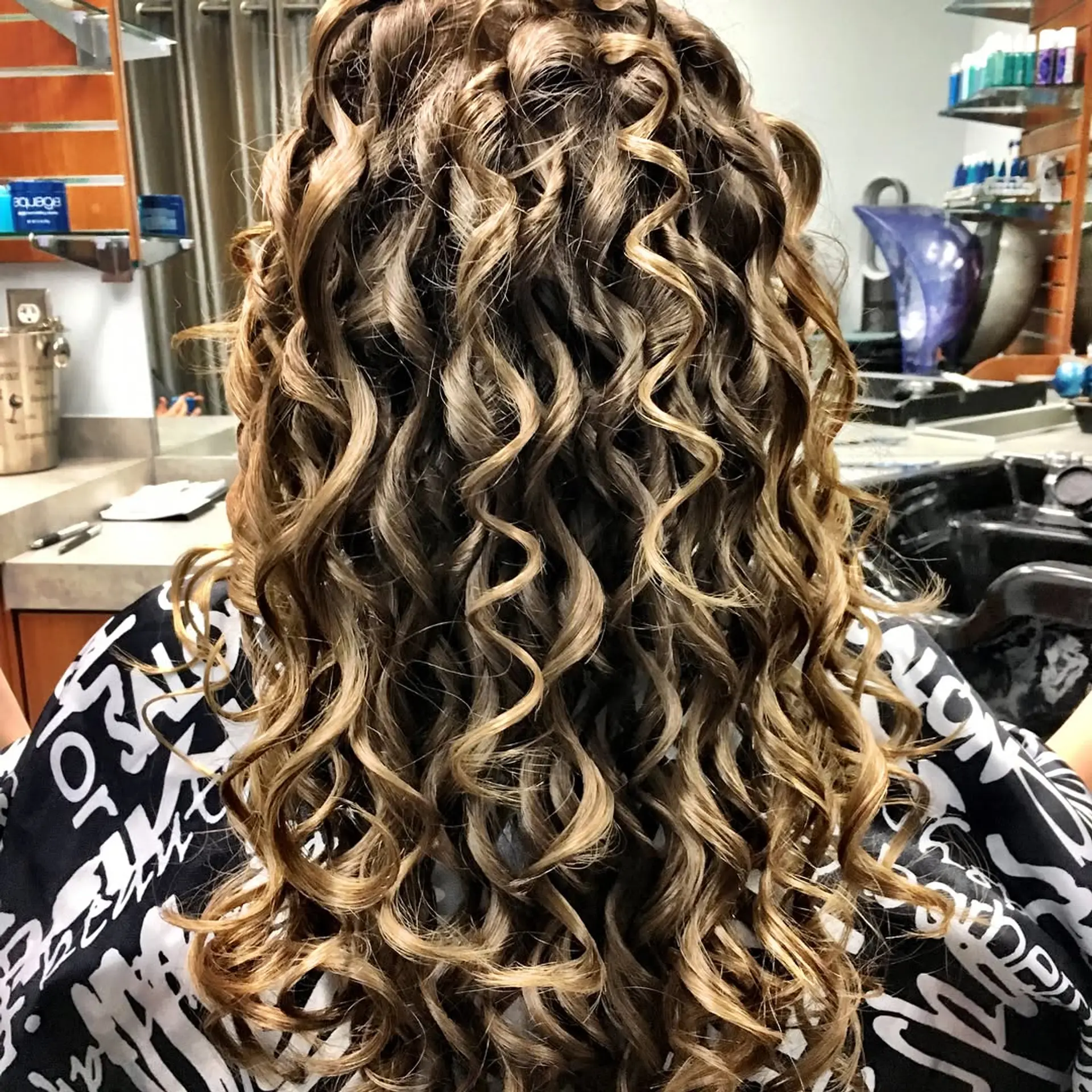 Long, dimensional brunette hair styled into defined and bouncy spiral ringlets with warm golden highlights. 1