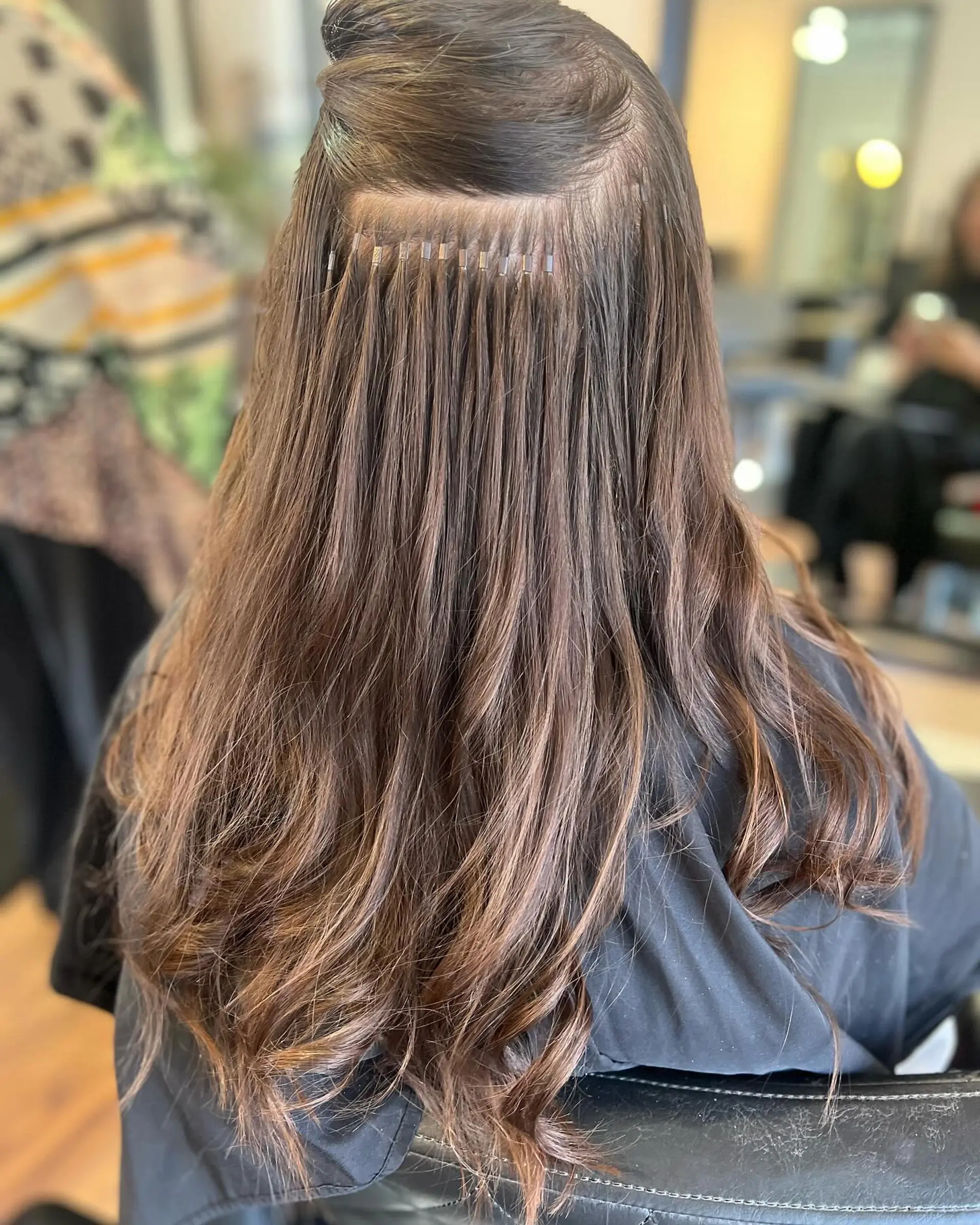 A precise row of micro-beaded I-tip hair extensions cleanly installed on brunette hair with soft wavy ends. 1