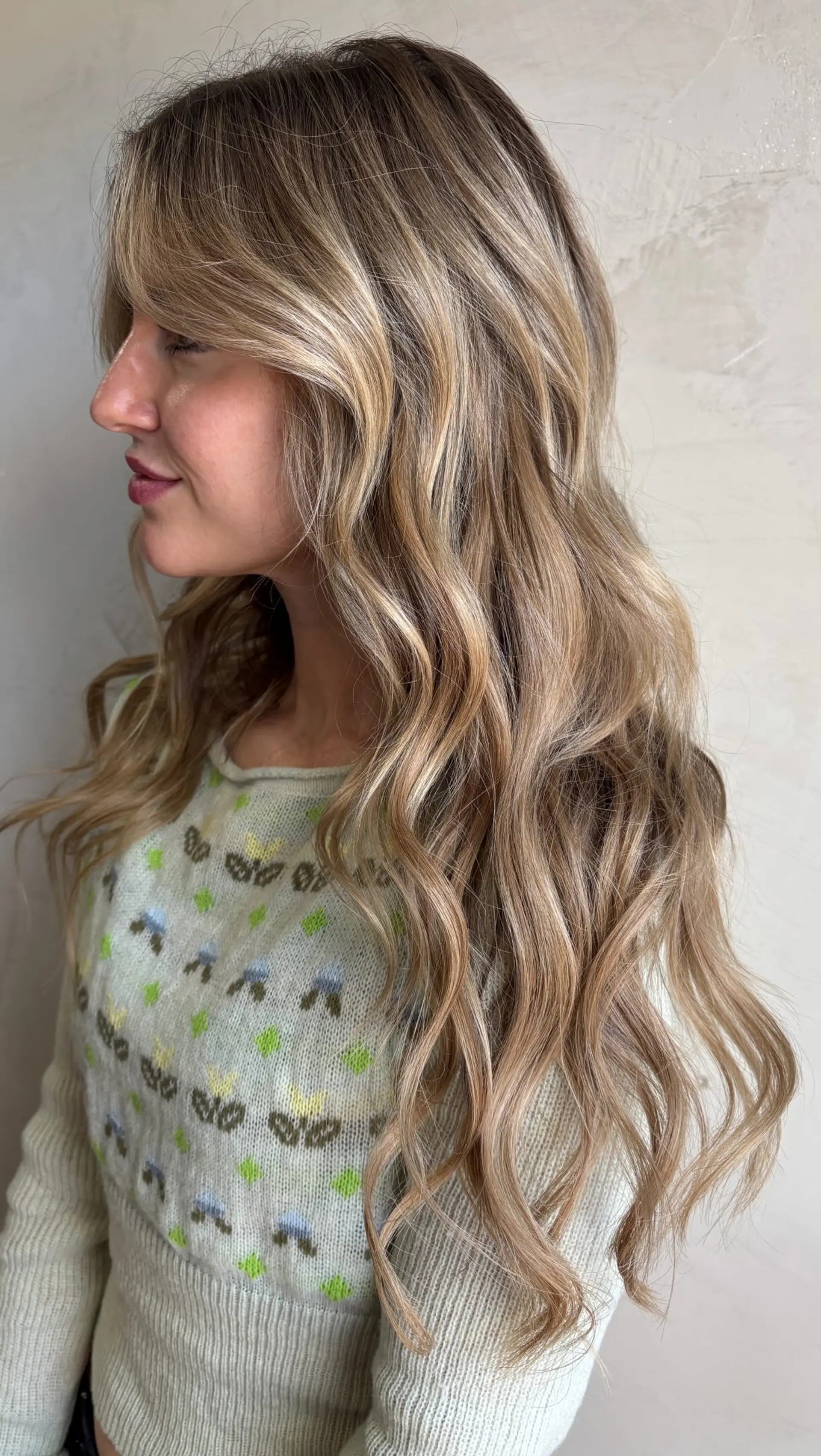 Long wavy dimensional blonde hair with soft curtain bangs framing the face. 1