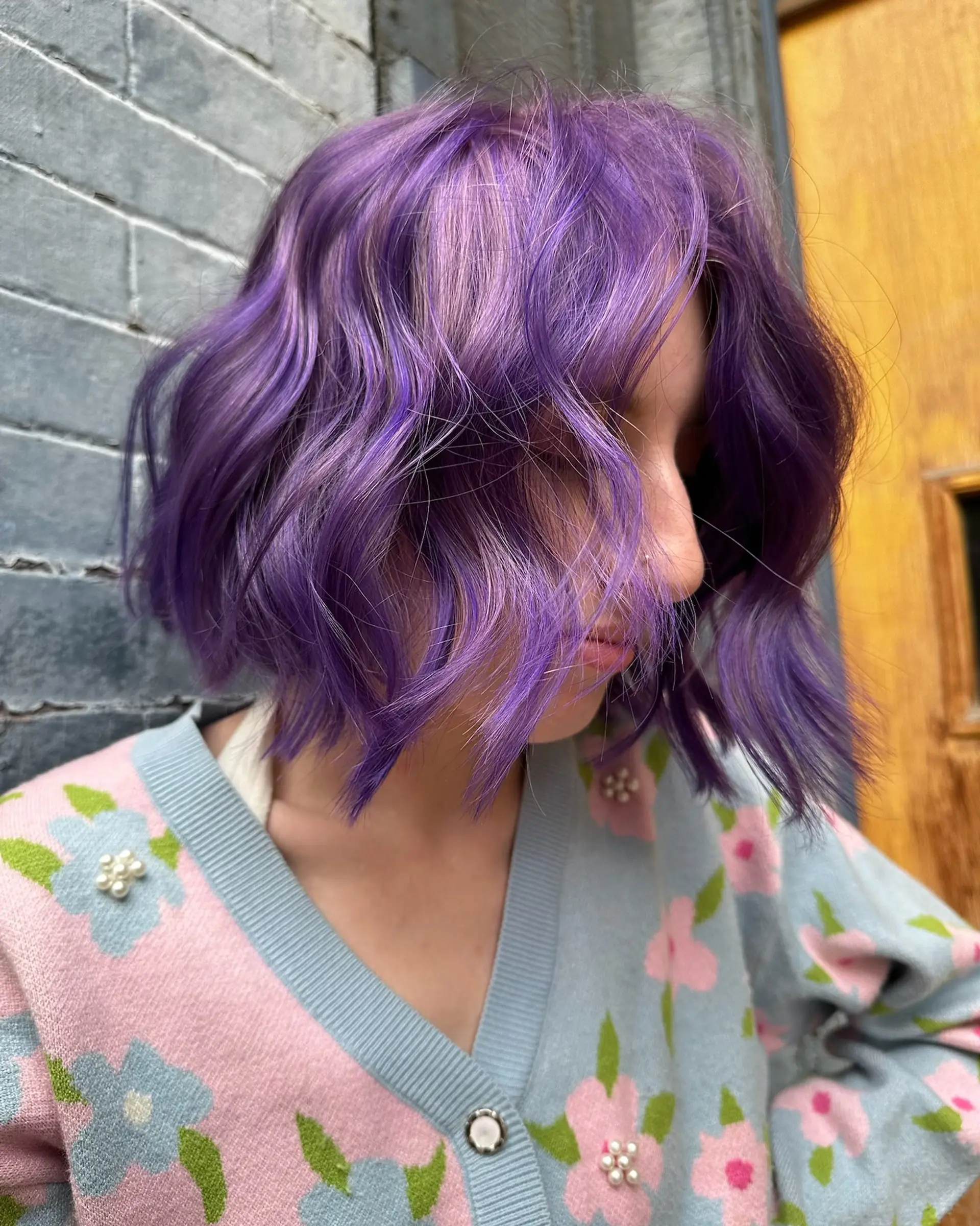 A textured chin-length bob styled with loose waves and colored in a vibrant, multi-tonal purple hue. 1