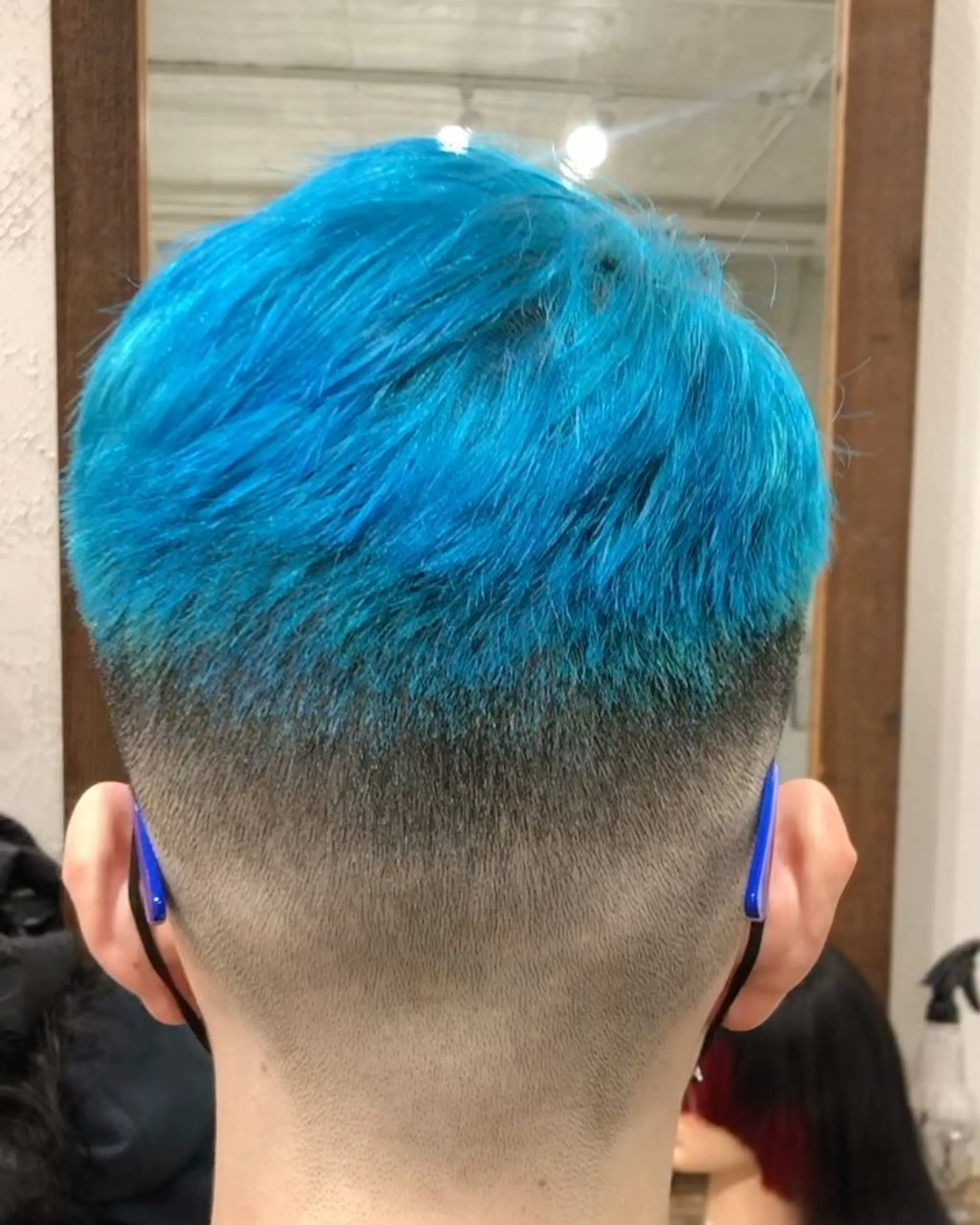 A bold and edgy hairstyle with straight, vibrant blue hair on top and a sharp fade transitioning to a natural black undercut, creating a modern contrast.