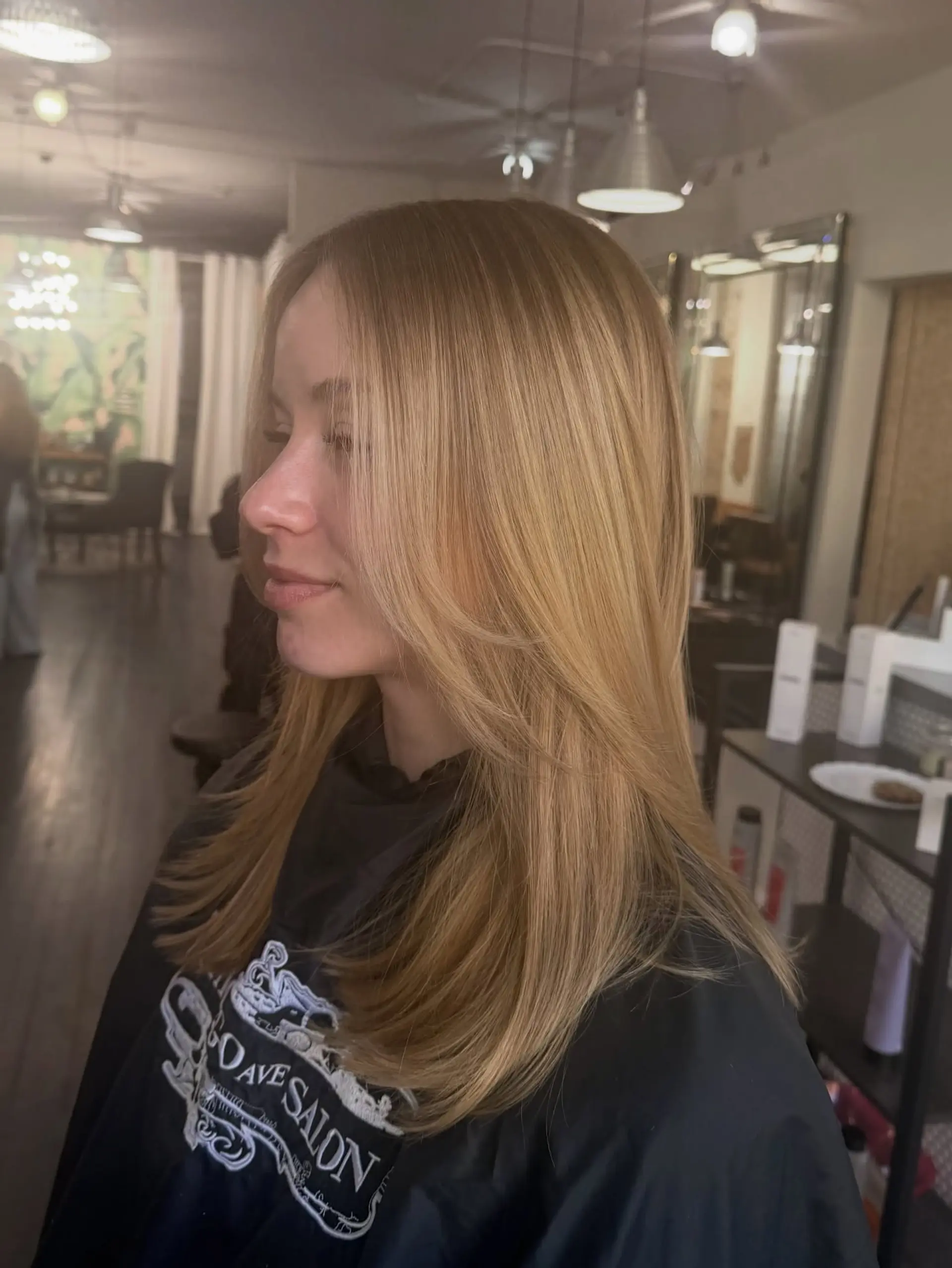 Long warm blonde hair cut with soft face-framing layers and styled with a smooth, rounded blowout. 1