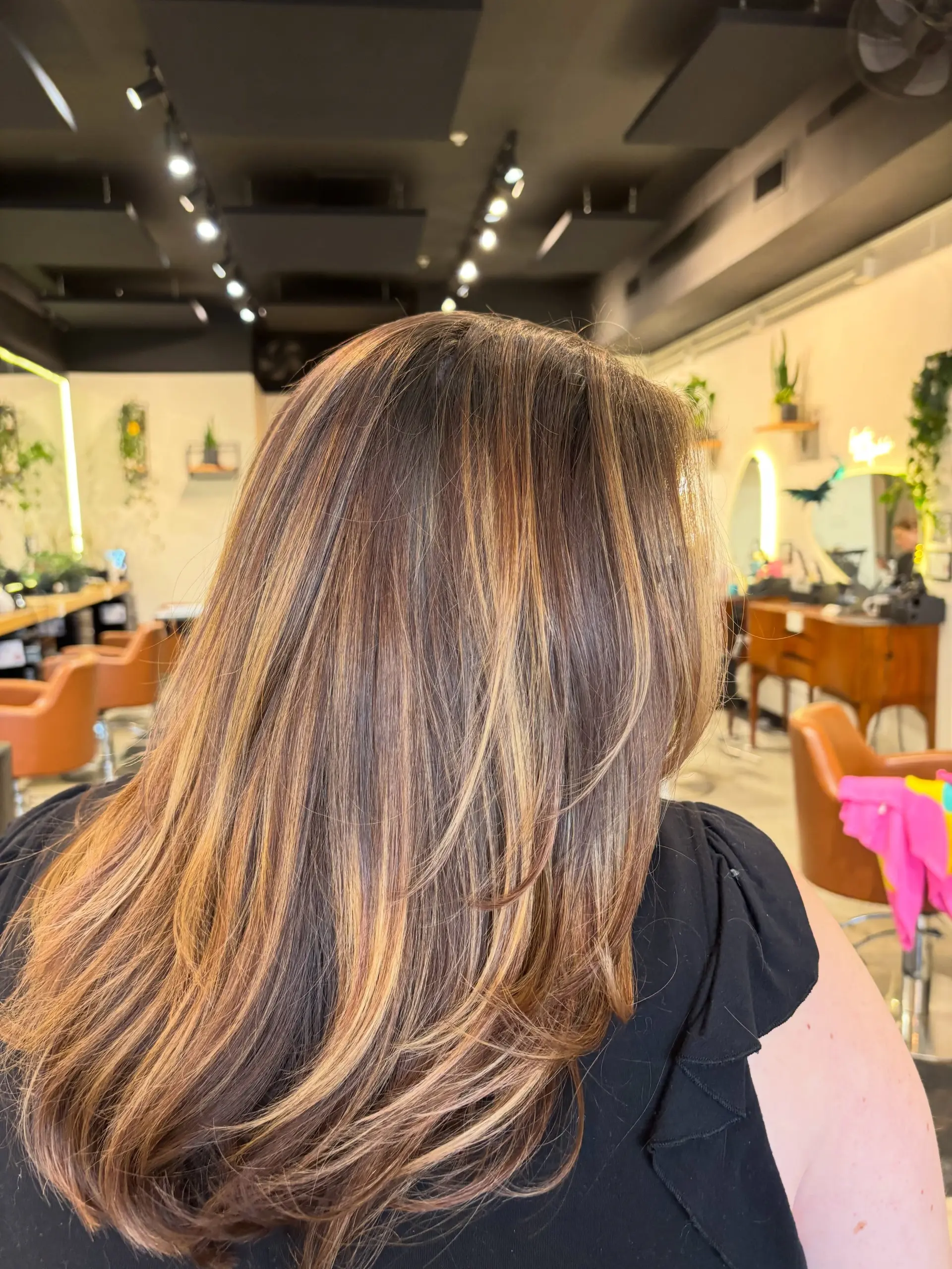 Long brunette hair styled with warm honey and caramel balayage highlights, face-framing layers, and a soft blown-out finish. 1