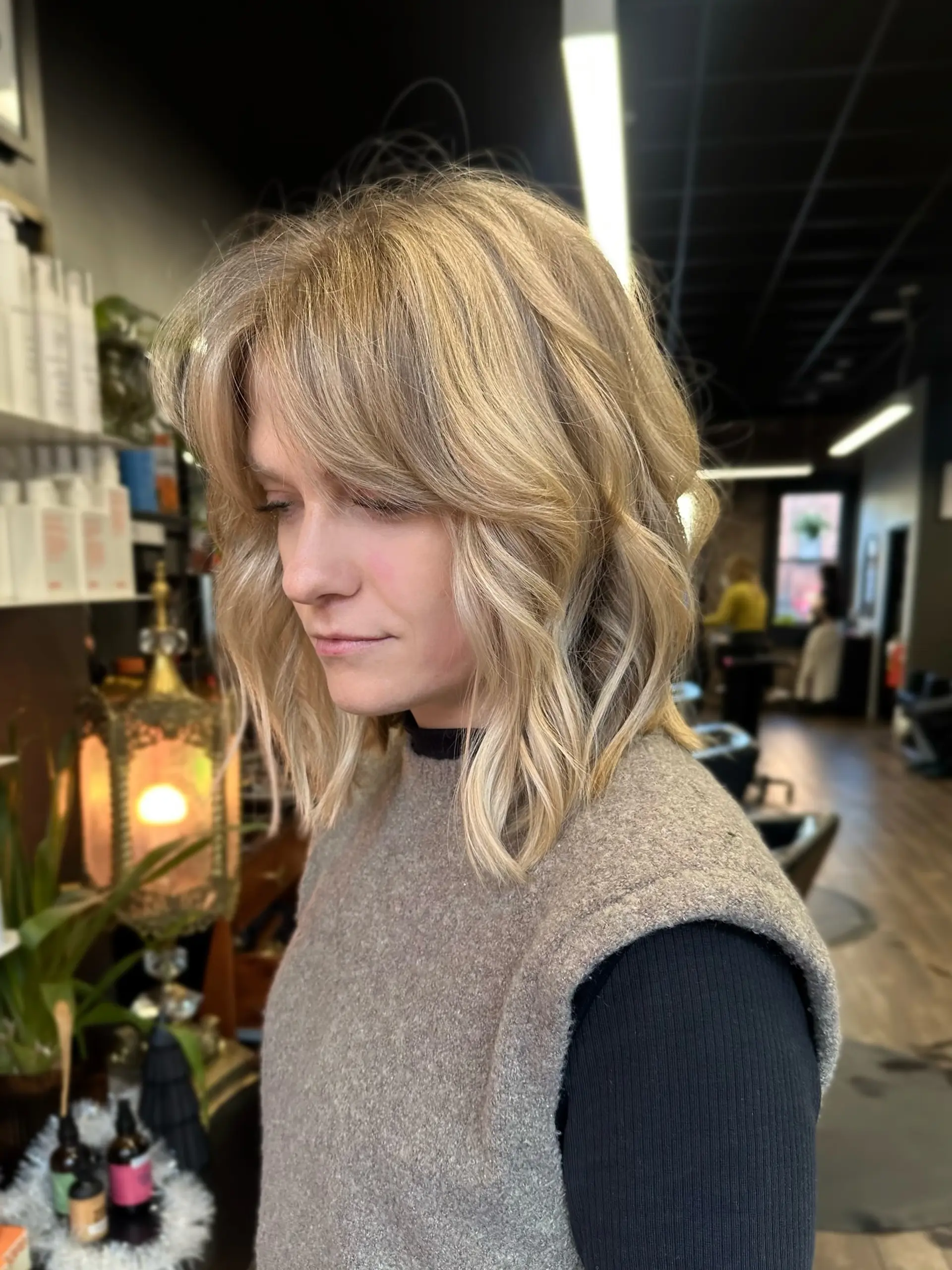 A textured shoulder-length blonde lob styled with loose waves and curtain bangs. 1