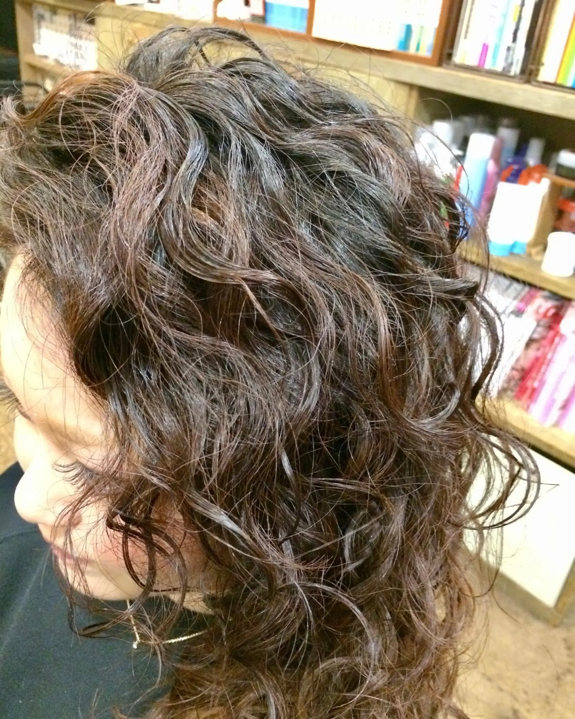 A medium-length hairstyle styled with defined spiral perm curls and a soft, textured finish. 1