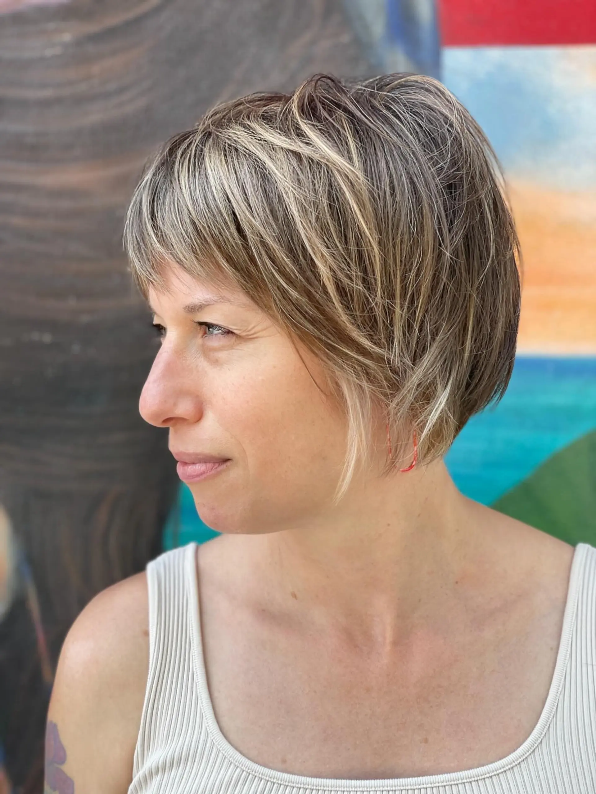 A textured short bob or bixie cut with piecey side-swept bangs, featuring dimensional blonde highlights woven through a natural light brown base. 1