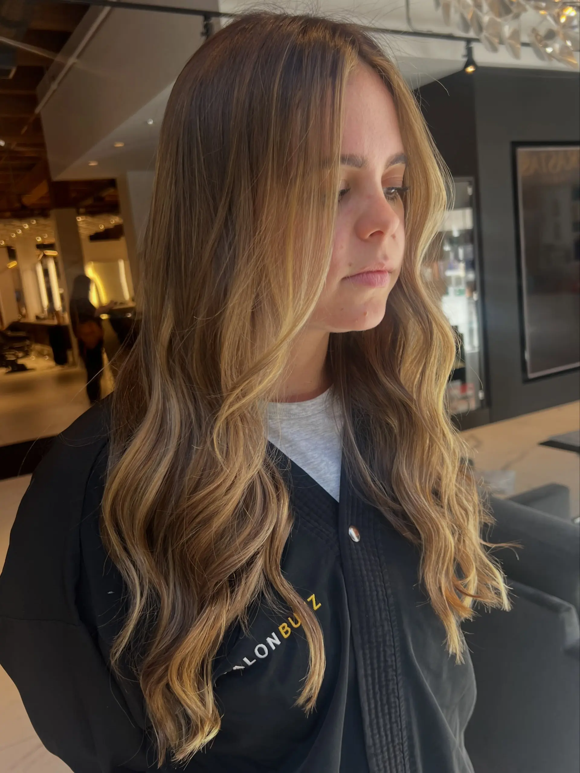 Long bronde hair featuring warm golden highlights blended into a brunette base, styled in loose cascading waves. 1