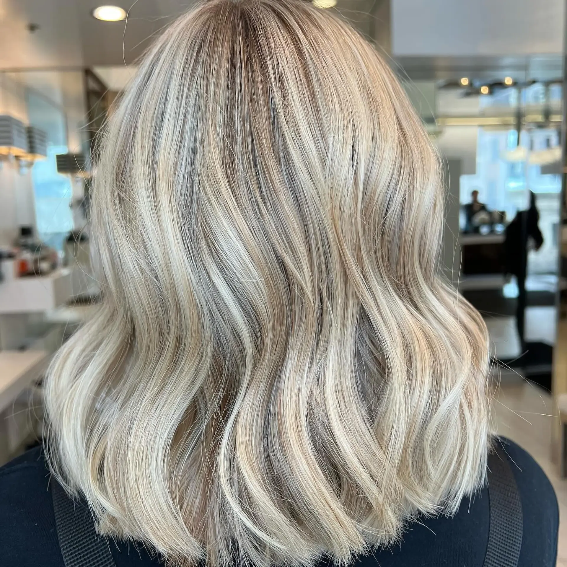 A medium-length textured blonde lob styled in soft, relaxed waves showcasing luminous blonde highlights. 1