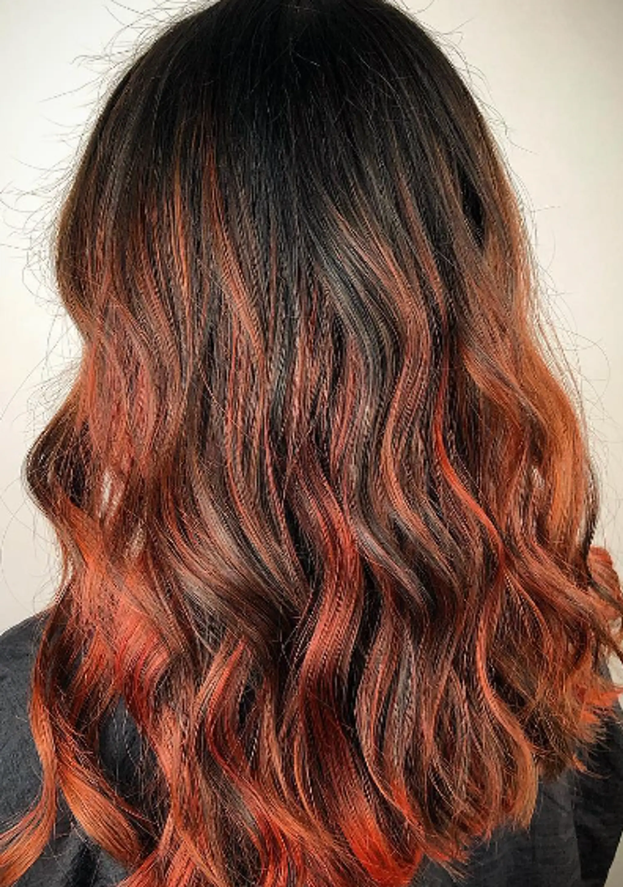 Medium-length, wavy hair with an ombre effect transitioning from black roots to red and orange tips, styled in loose, natural waves.