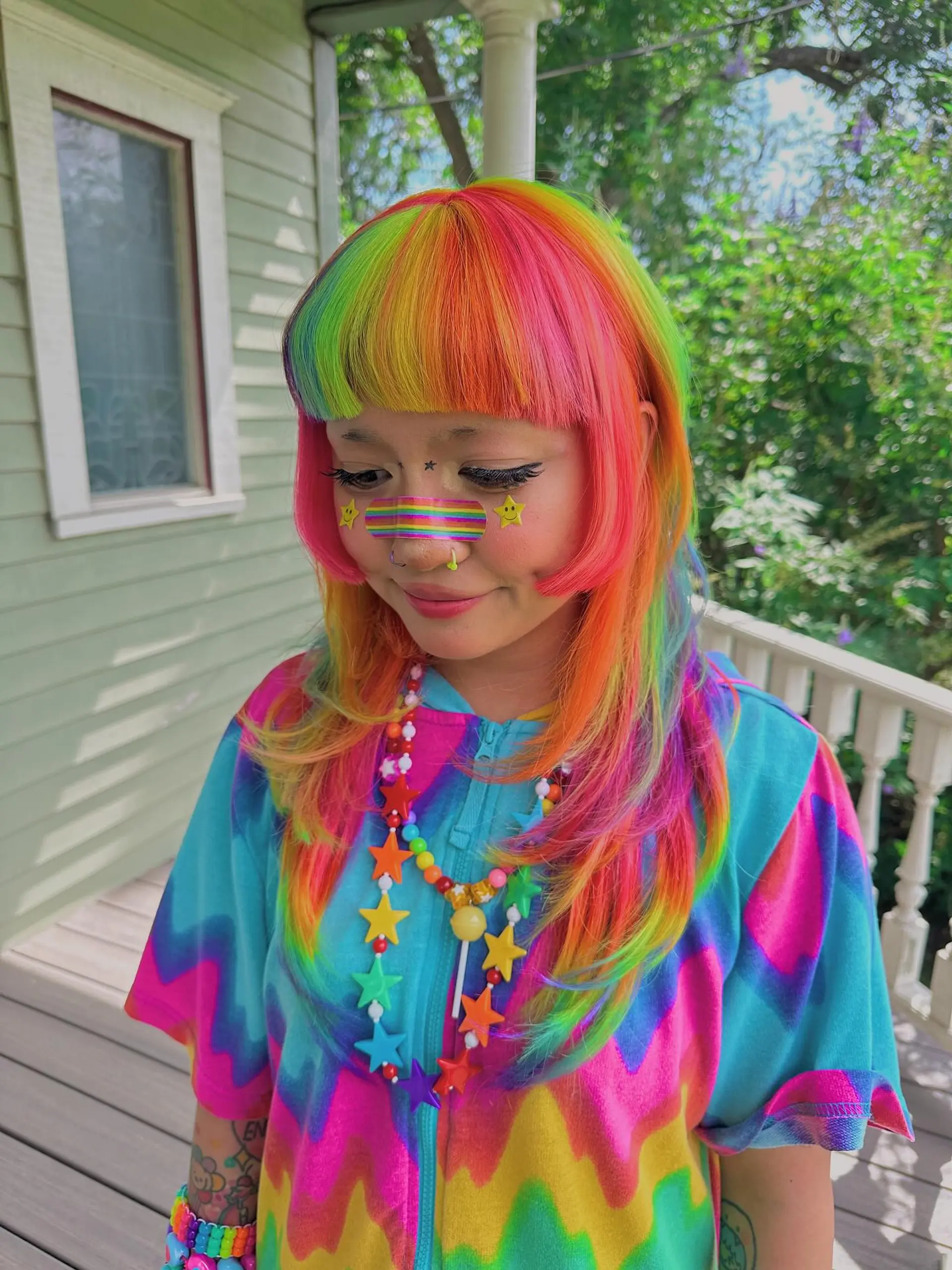 A medium-length hairstyle with vibrant rainbow coloring, characterized by sharp blunt bangs and soft face-framing layers that create a contemporary shag silhouette. 1