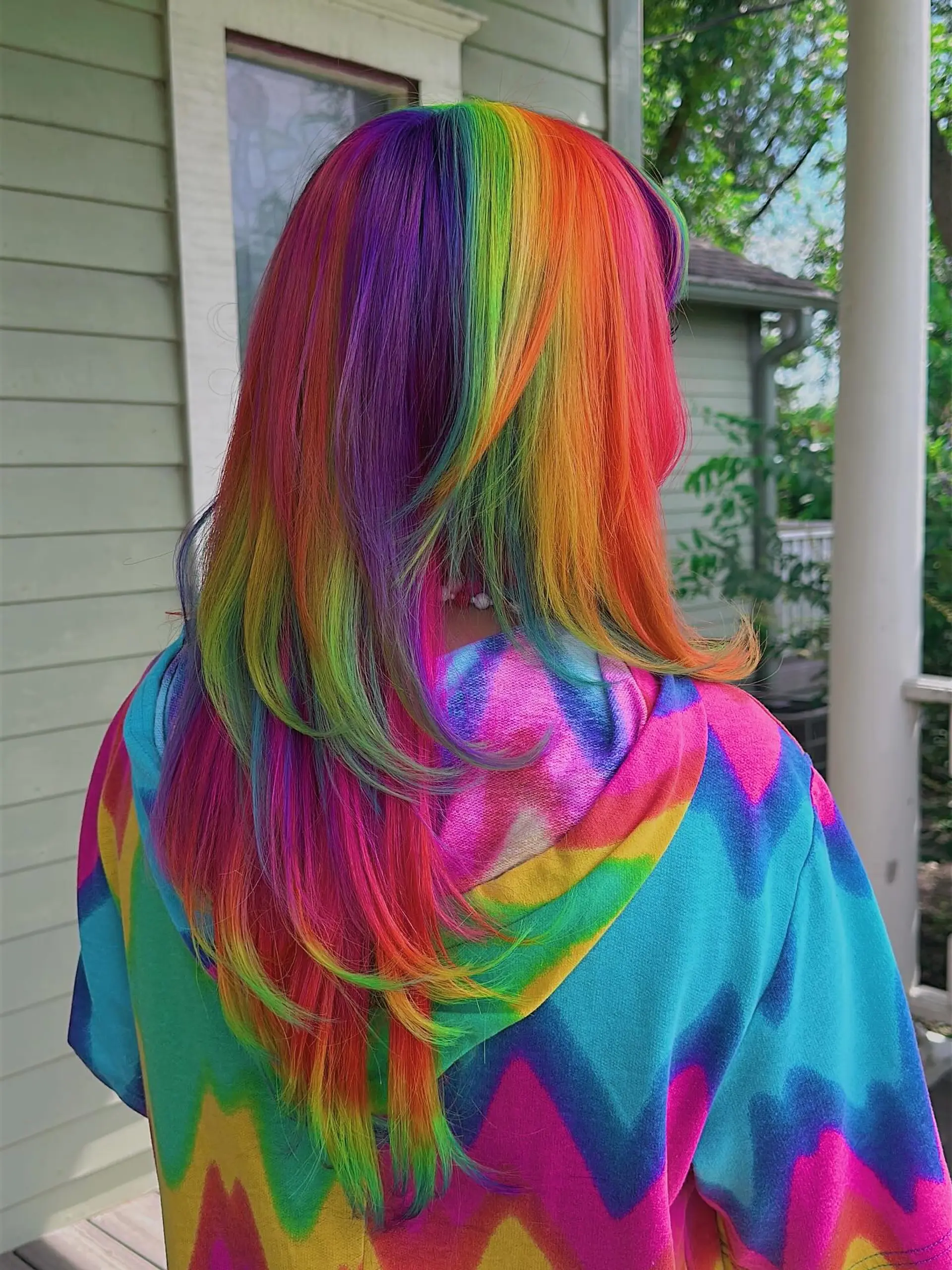 A medium-length hairstyle with vibrant rainbow coloring, characterized by sharp blunt bangs and soft face-framing layers that create a contemporary shag silhouette. 2
